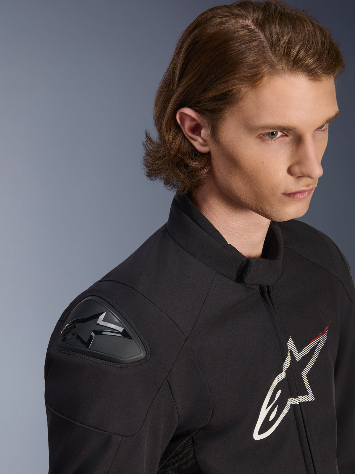 Alpinestars SMX Vandtæt Jakke, sort med hvide og røde detaljer, tæt på lifestyle-billede af en mandlig model, med eksterne DFS Lite-skulderglidere og et stort stjernelogo på brystet, sportsmotorcykelbeklædning