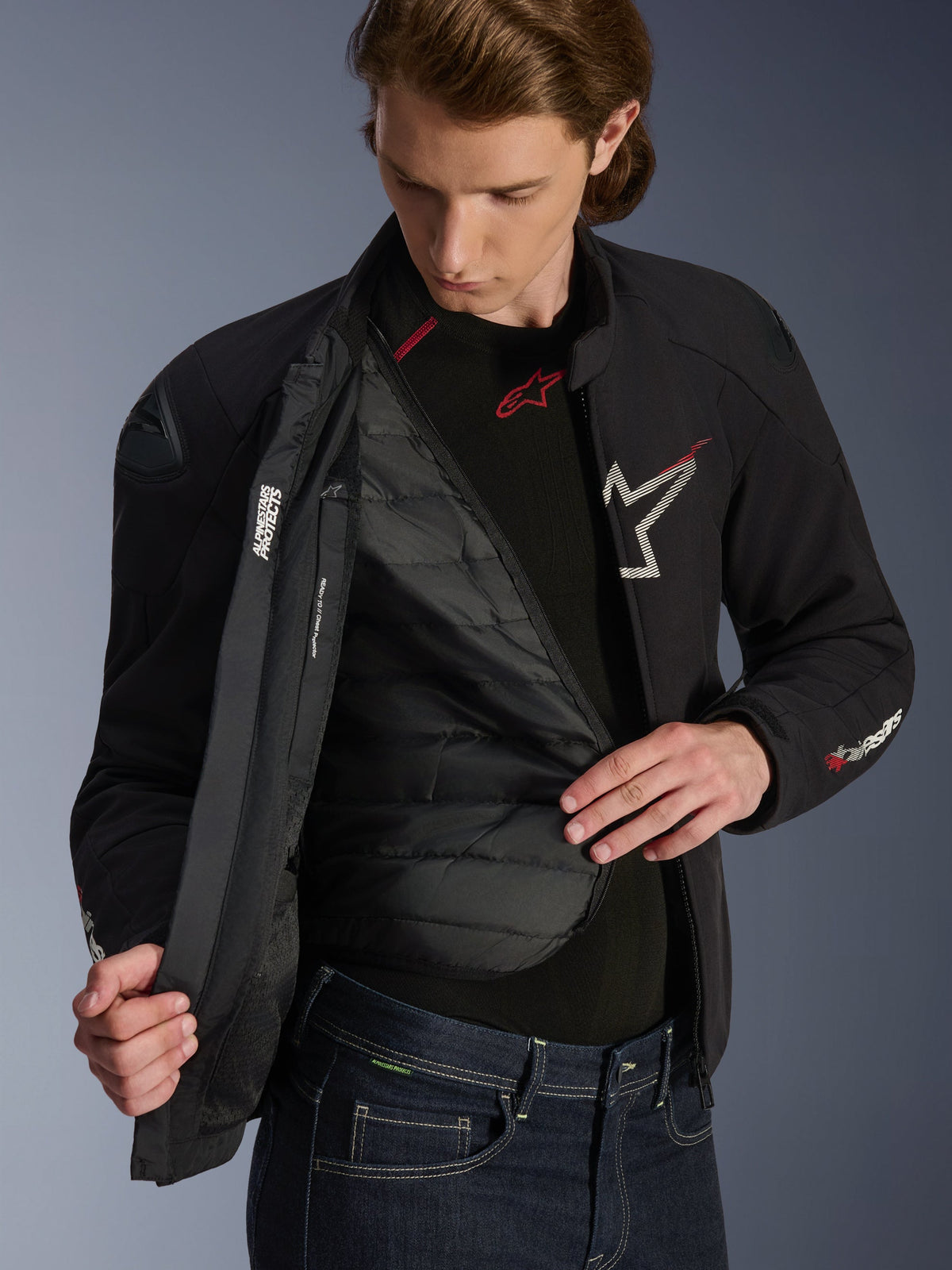 Alpinestars SMX vandtæt jakke i sort, hvid og klar rød, bæres af en mand og er lynet op for at vise den quiltede, aftagelige termoforing, med eksterne DFS lite-skuldre og hvide logodetaljer, højtydende motorcykeludstyr til vejbrug