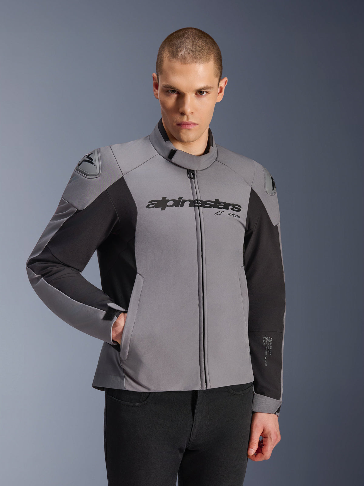 Alpinestars SMX vandtæt jakke, mørkegrå og sort, båret af en mandlig model, med 'alpinestars'-branding på brystet, DFS Lite-skulderbeskyttelse, strømlinet sportsdesign med tekstil- og softshell-materialer til vejridning.