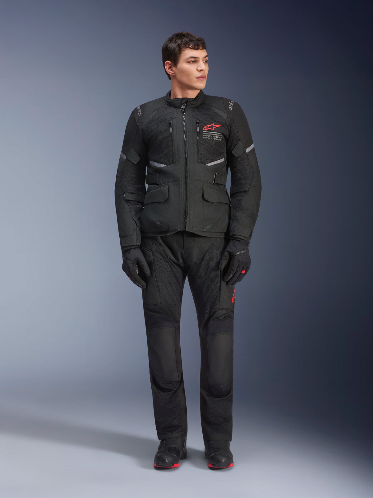Mandlig model iført Alpinestars Andes Air Drystar® jakke i sort, adventure touring-motorcykeludstyr med matchende bukser og handsker, rødt logo på brystet, mesh-ventilation og funktionelle lommer.