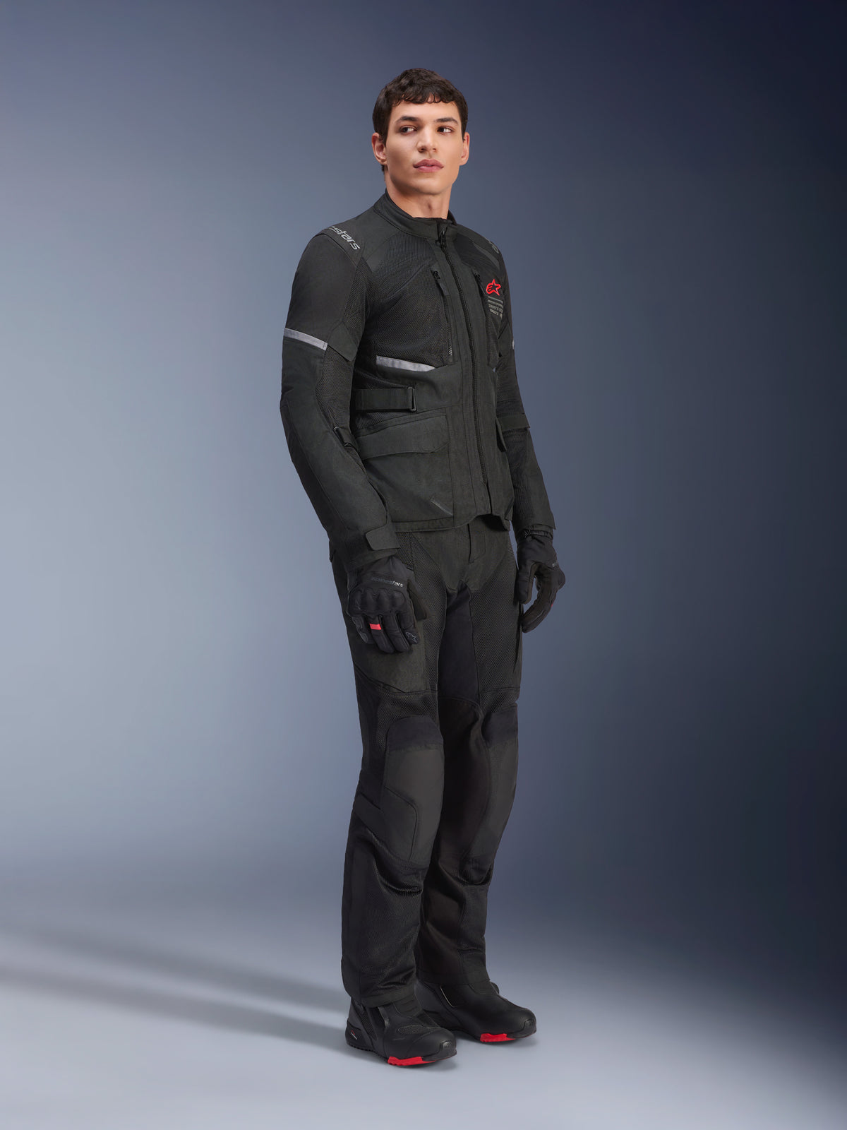 Alpinestars Andes Air Drystar®-jakke, sort, båret af en model som del af et komplet adventure-outfit til motorcykel med matchende bukser, handsker og støvler, mesh-ventilationspaneler, rødt logo på brystet og refleksstriber.