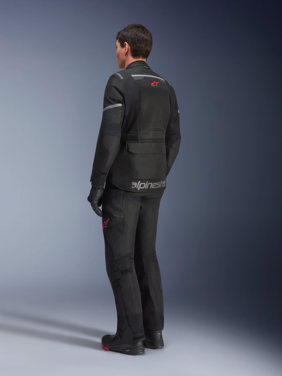 Alpinestars Andes Air Drystar®-jakke, sort, set bagfra på en kører, med omfattende mesh-paneler til ventilation, båret med matchende adventure motorcykelbukser og støvler, viser det vejorienterede touring-design og branding.