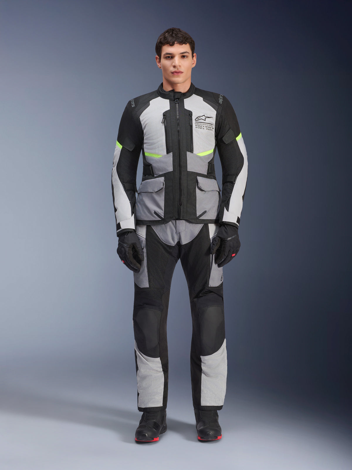 Alpinestars Andes Air Drystar® Jacket in Ice Gray, Dark Gray, and Black, worn by a male model with matching riding pants and gloves, adventure touring design featuring large front pockets and fluorescent yellow accents, studio front view