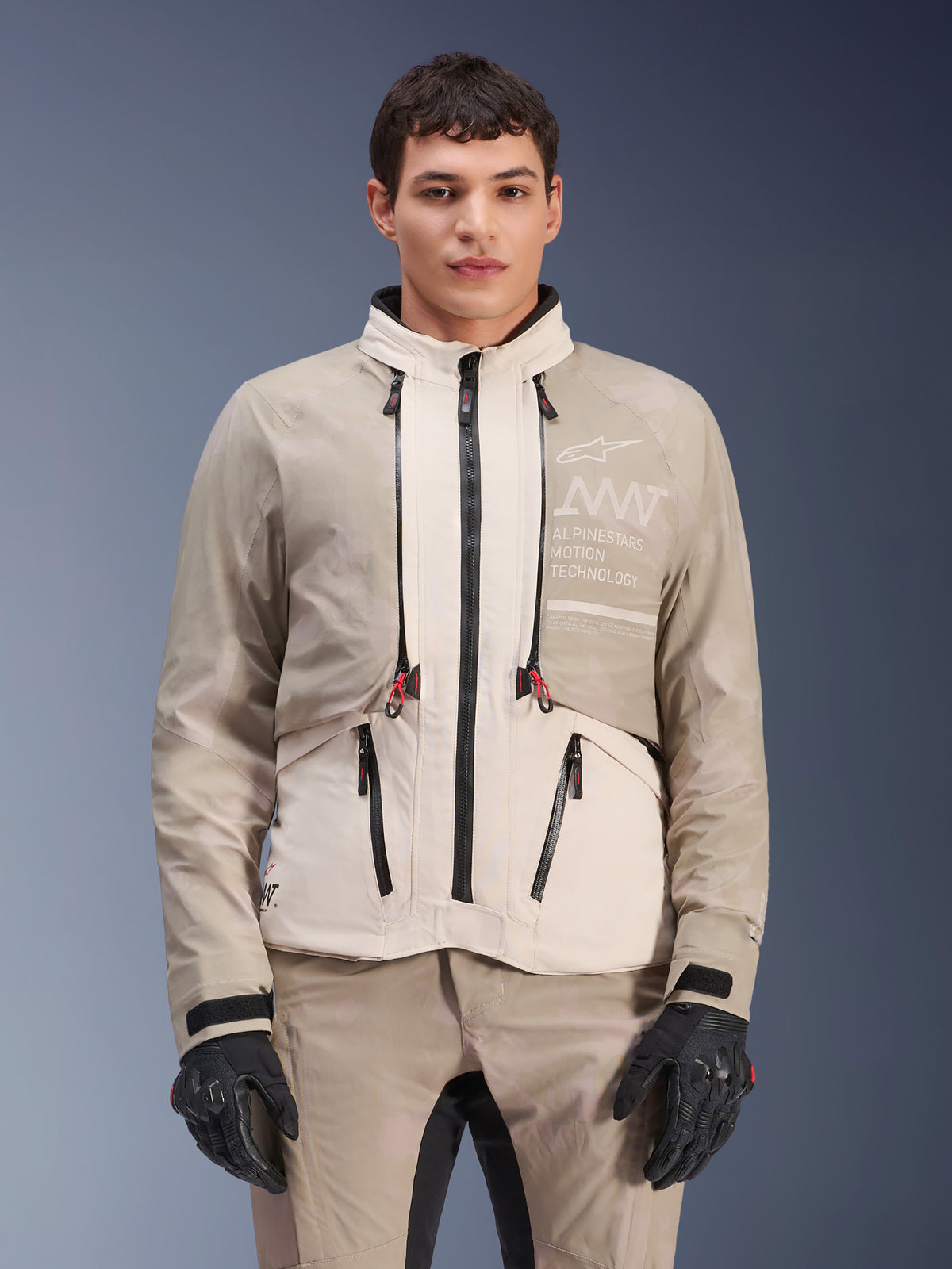 Alpinestars AMT-10LAB Drystar® XF Jacket, Adventure Motorcycle Jacket, White Sand Aluminum Camo, modular design with black zippers and red accents, worn with matching pants and black gloves, featuring Alpinestars Motion Technology branding on the chest, professional all-weather riding suit