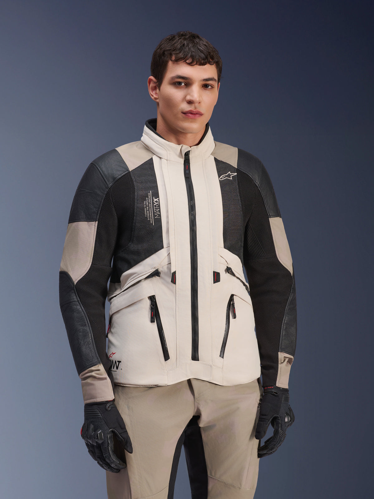Alpinestars AMT-10LAB Drystar® XF Jacket, White Sand Aluminum Camo, motorcycle adventure jacket with black MATRYX® mesh panels and leather reinforcements, worn by a model with black gloves and matching sand-colored pants, studio portrait