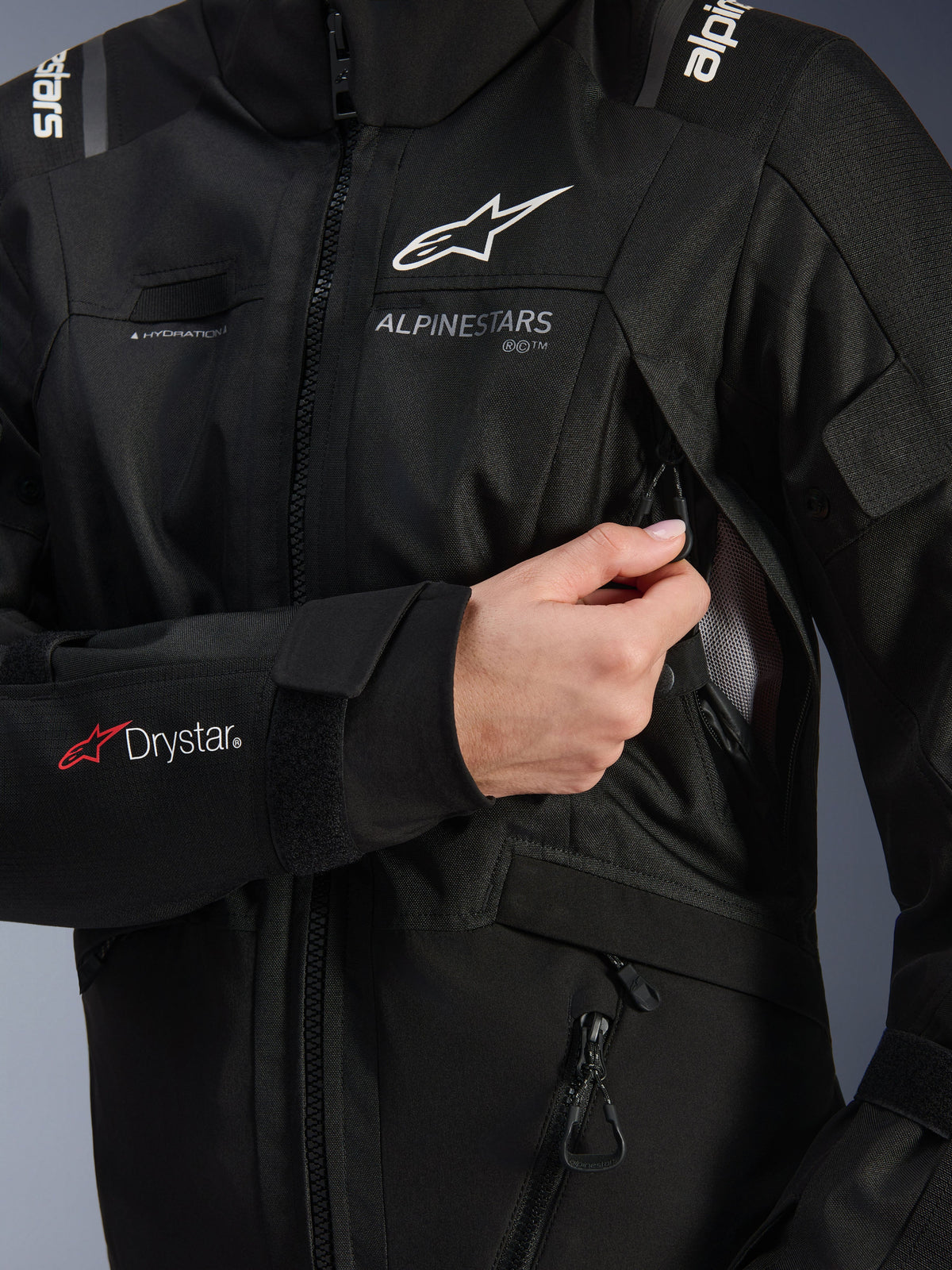 Alpinestars Stella Andes V4 Drystar® jakke til kvinder, sort, detaljebillede der viser brystventilationsindtaget blive åbnet, med mesh-foring, Drystar®-logo på underarmen og løkke til hydreringsslange, teknisk motorcykelbeklædning.
