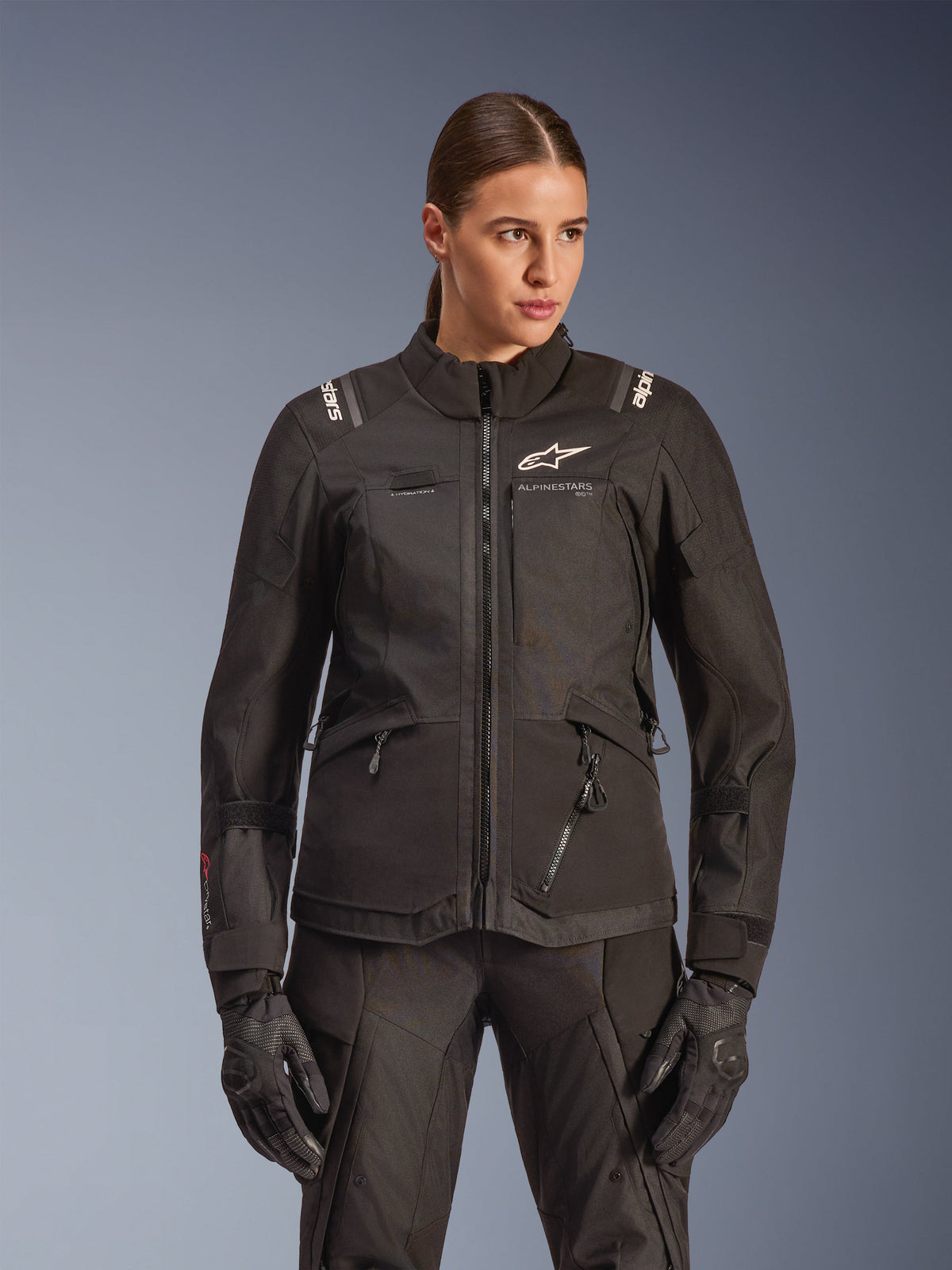 Alpinestars Stella Andes V4 Drystar-jakke, motorcykel-touringjakke til kvinder, sort, båret af en model med matchende kørebukser og handsker, med lynlåslukning foran, hvidt logo på brystet og Alpinestars-branding på skuldrene, elegant altvejrsudstyr.