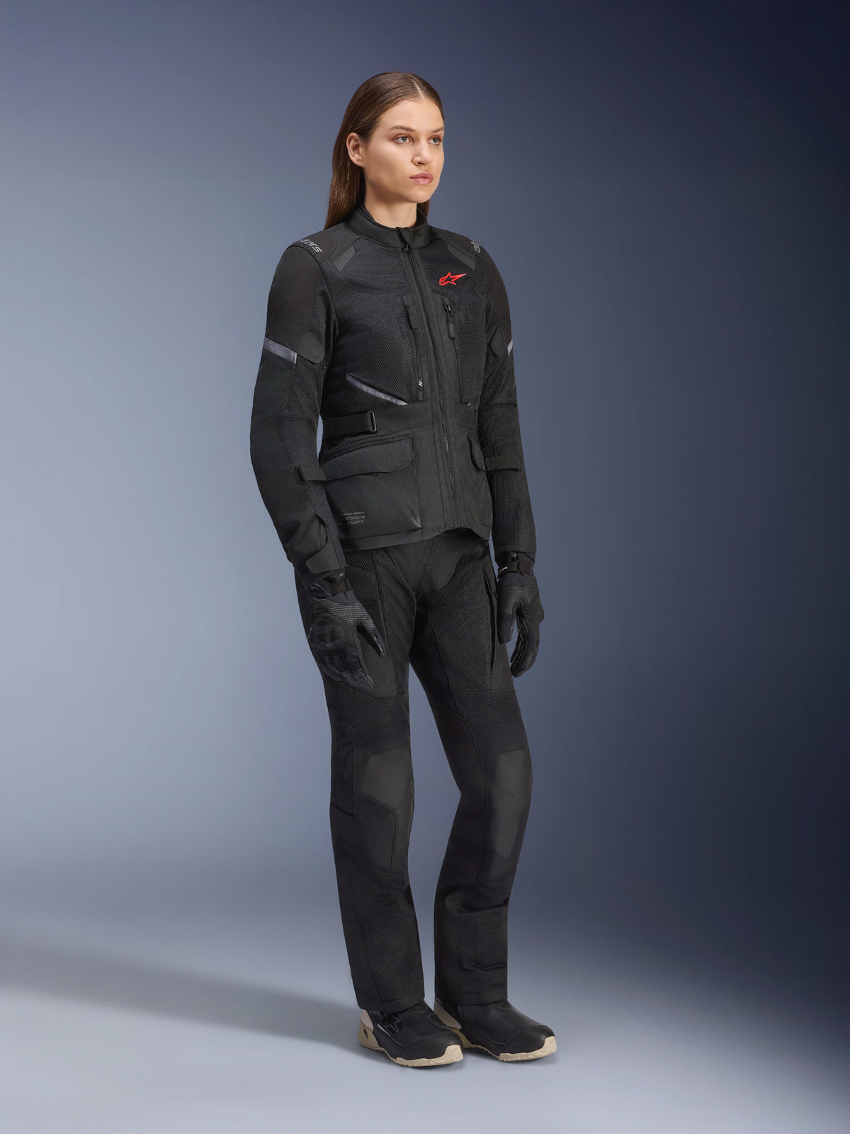 Kvinde iført Alpinestars Stella Andes Air Drystar®-jakke, sort adventure-touringjakke i tekstil, båret med matchende sorte bukser og handsker, med store mesh-ventilationspaneler og et rødt logo, koordineret outfit til motorcykelkørsel til kvinder