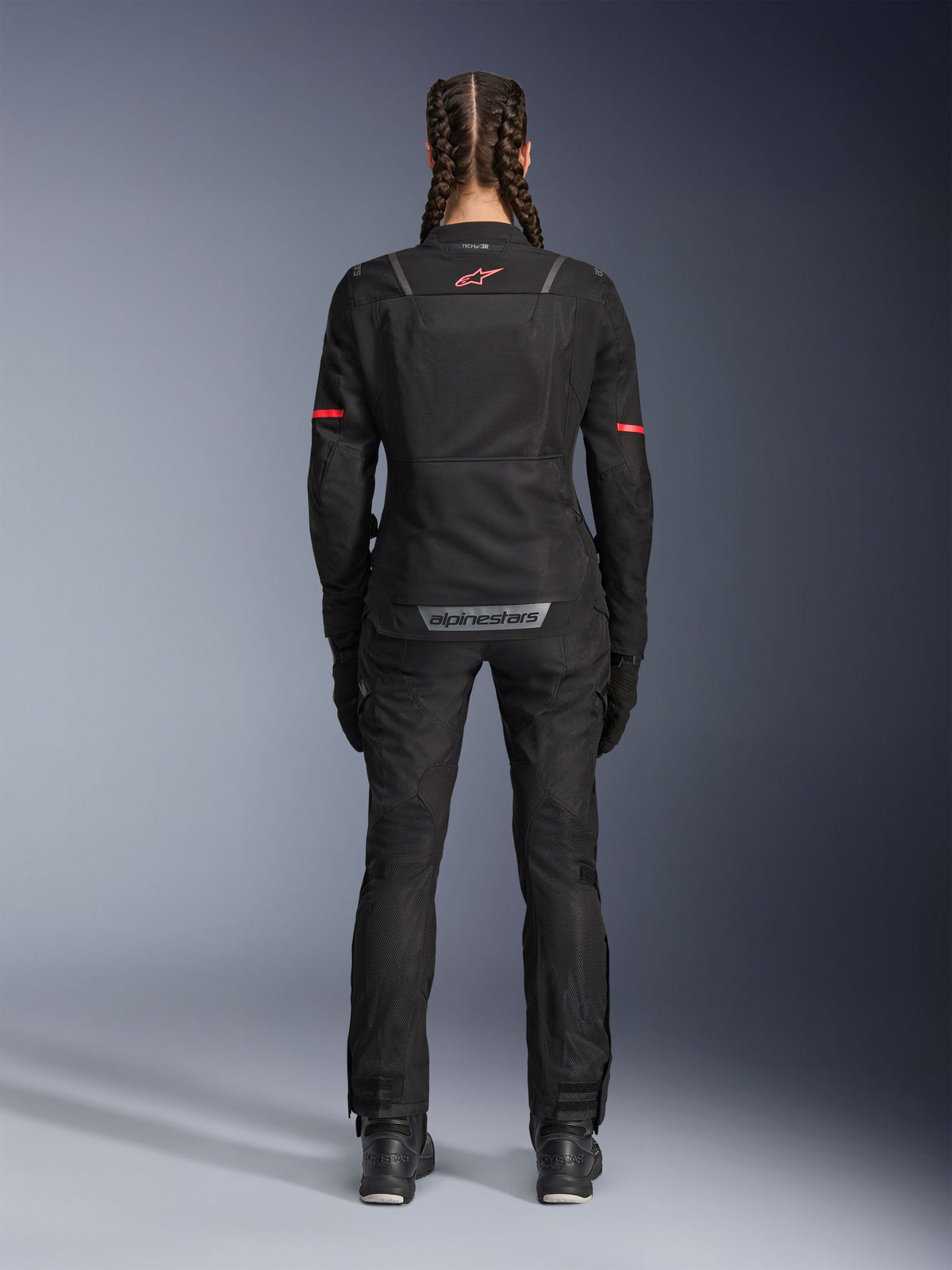 Alpinestars Stella ST-2 Air jakke, motorcykeljakke til damer, sort, set bagfra med rødt logo på øverste del af ryggen og gråt branding på nederste del af ryggen, båret med matchende sorte kørebukser og støvler, moderne touring-design med mesh-paneler og reflekterende detaljer