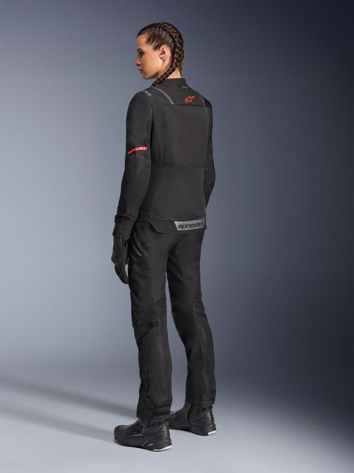 Alpinestars Stella ST-2 Air-jakke, motorcykeljakke til damer, sort med røde detaljer på ærmer og øverste del af ryggen, set bagfra på model iført matchende sorte motorcykelbukser og støvler, med reflekterende Alpinestars-branding og moderne tekstilkonstruktion.