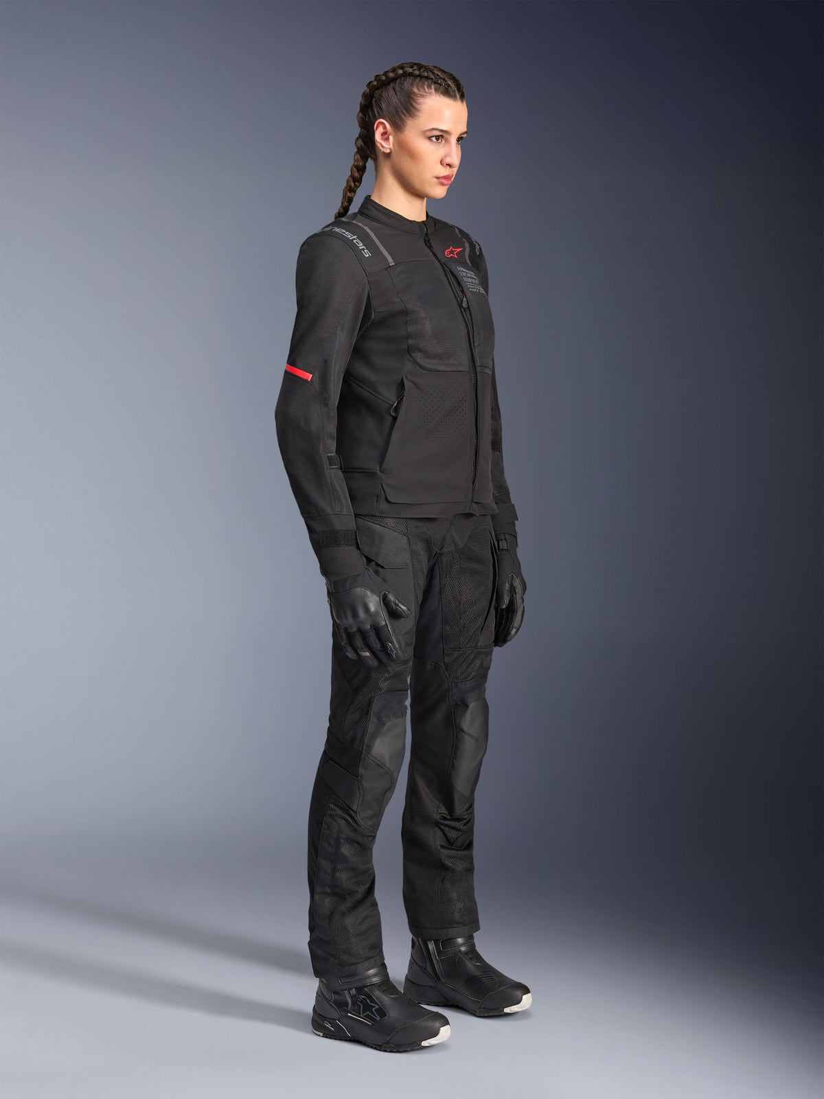 Kvindelig model iført Alpinestars Stella ST-2 Air Jakke i sort, kombineret med matchende sorte motorcykelbukser, handsker og støvler, mesh-ventilationspaneler og subtile røde detaljer, stilfuldt moderne touring-outfit