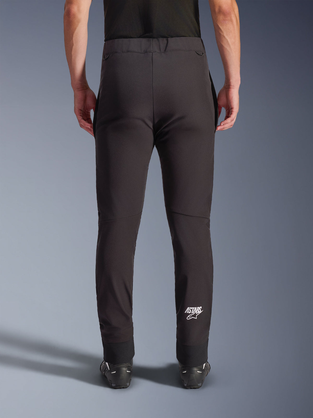 Alpinestars Aeroshel l bukser, sorte sof tshell motorcykelbuk ser, set bagfra med tætsiddende pasform og forbuede knæ, hvi dt Astars-logo på n ederste højre læg, e lastisk kant forned en, crossover-desig n til kørsel på vej