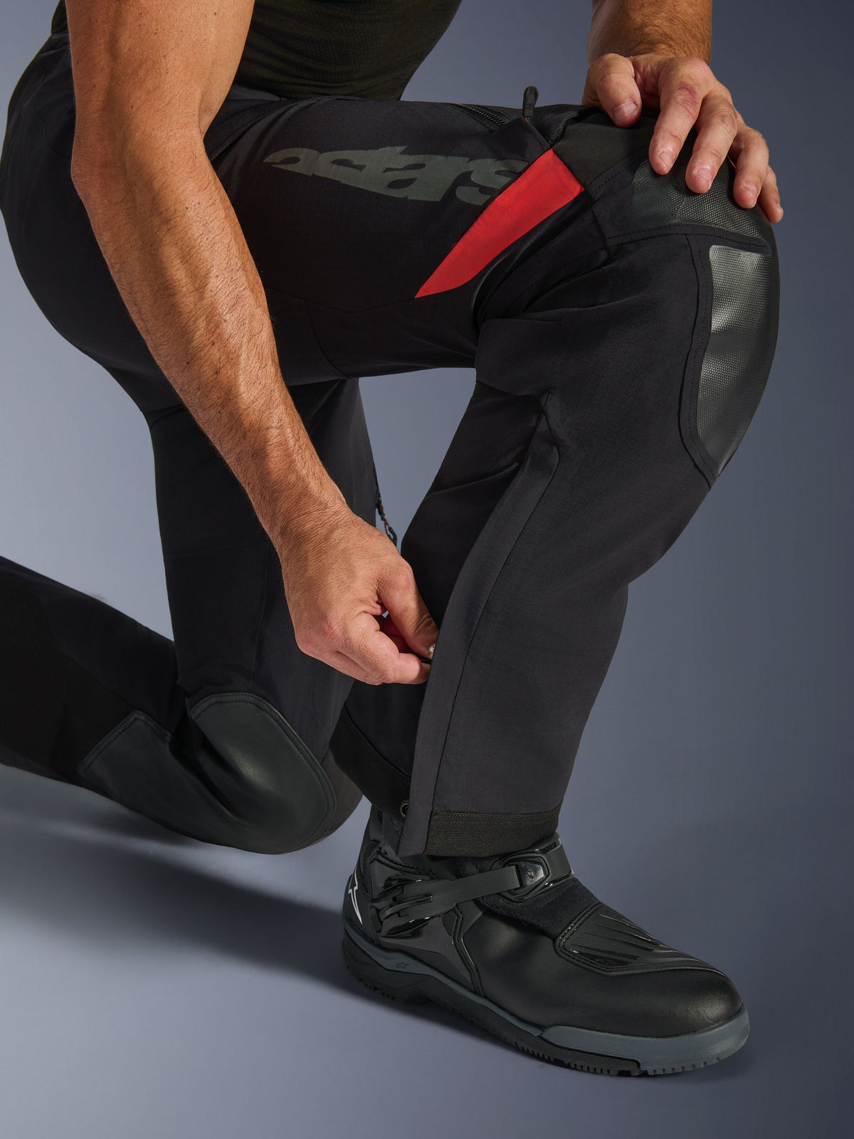 Alpinestars Halo Pro Drystar® XF Laminated Pants, Black Dark Shadow, close-up of lower leg with adjustable calf zipper, featuring durable knee reinforcements, red accents, and 'astars' branding, worn with black motorcycle boots.