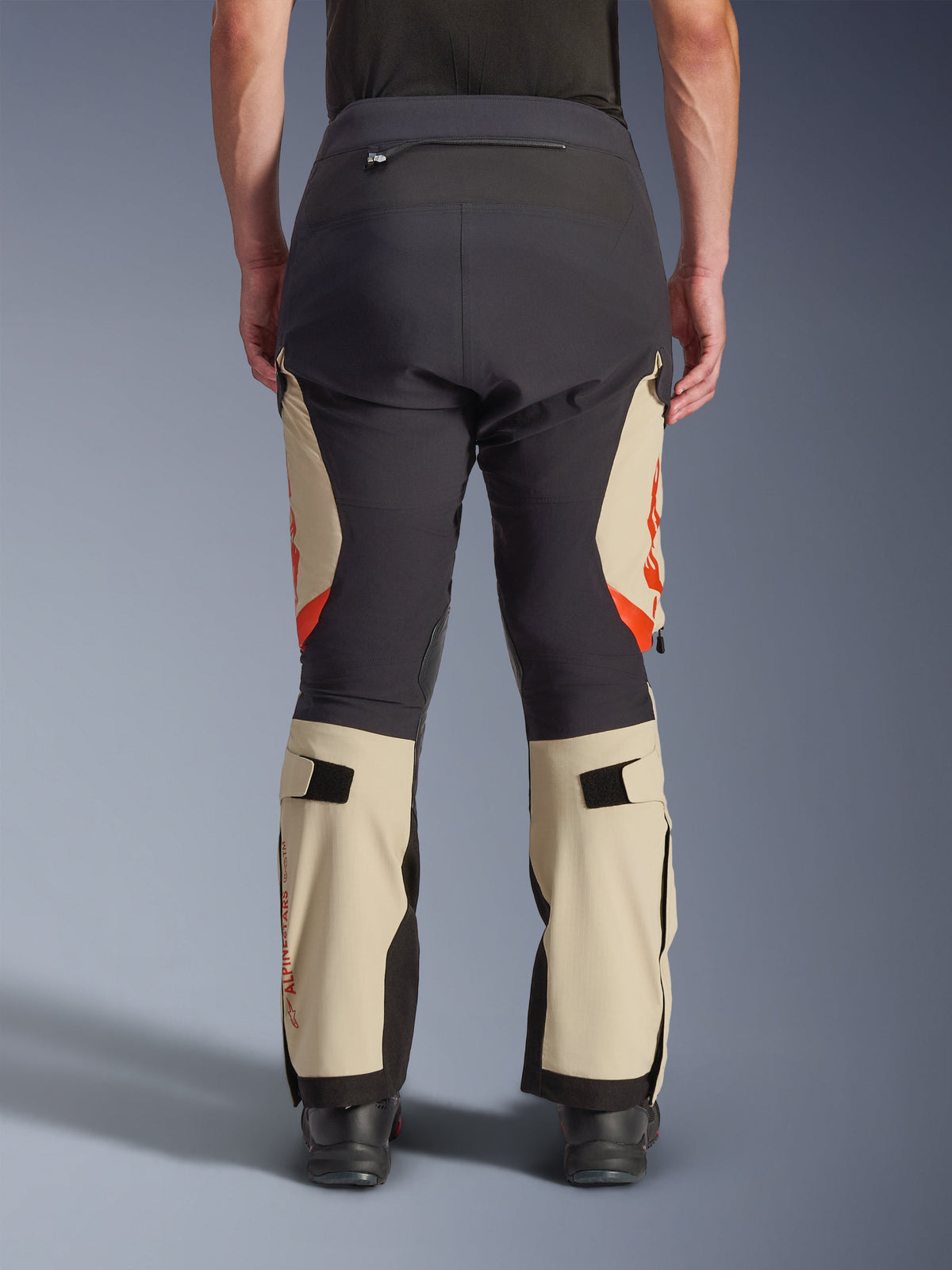 Alpinestars Halo Pro Drystar® XF laminerede bukser set bagfra, Mastic Black med beige paneler og orange detaljer, adventure-motorcykelbukser i teknisk tekstilkonstruktion, båret med sorte kørestøvler