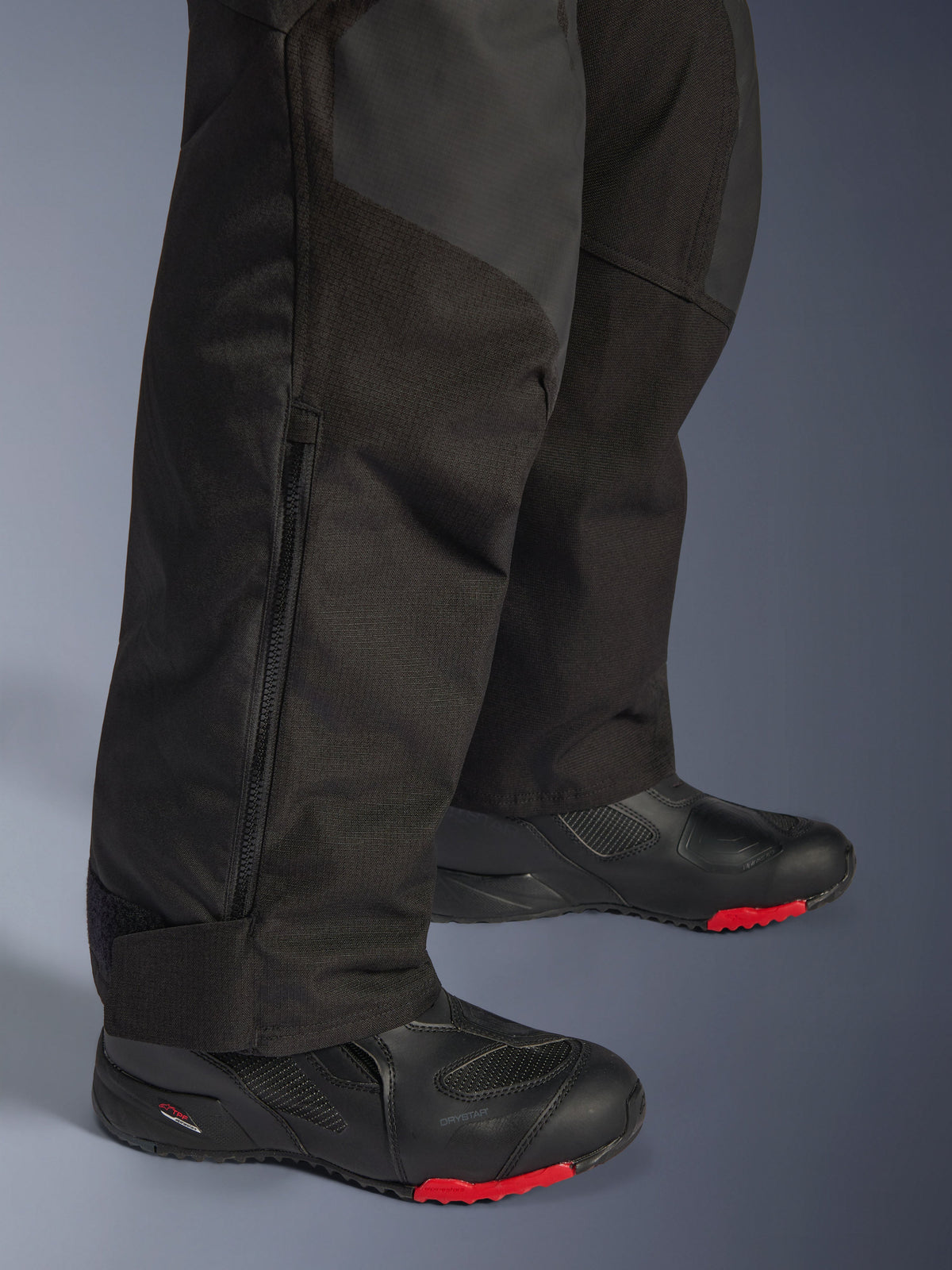 Alpinestars Andes V4 Drystar® bukser - Short, sort, nærbillede af detalje på underbenet, der viser tekstilkonstruktion, lodret lynlås til ventilation og justerbare ankelmanchetter, båret med sorte motorcykelstøvler