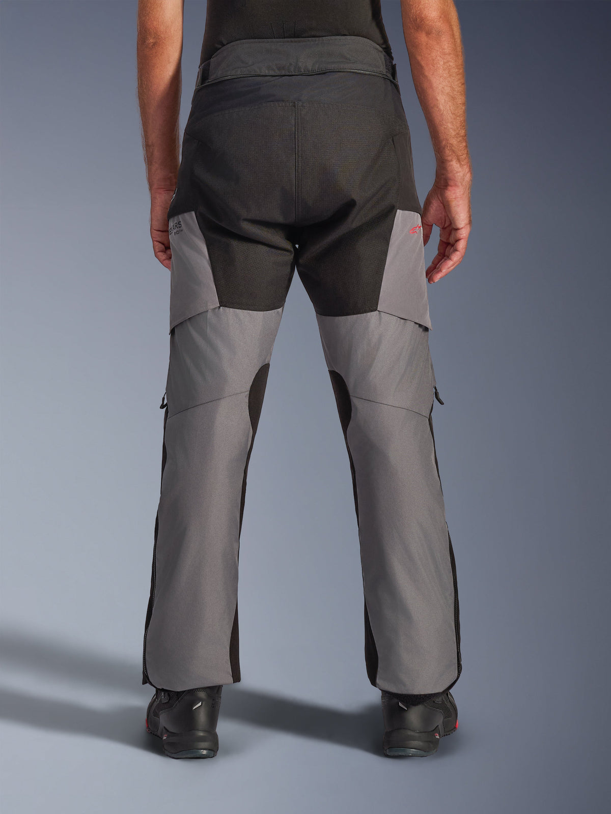 Alpinestars Andes V4 Drystar® bukser, adventure-motorcykelbukser, sort og mørkegrå, set bagfra med forstærket sort sæde og grå ben, lille rødt logo, kombineret med sorte kørestøvler, slidstærk tekstilkonstruktion til touring i al slags vejr.