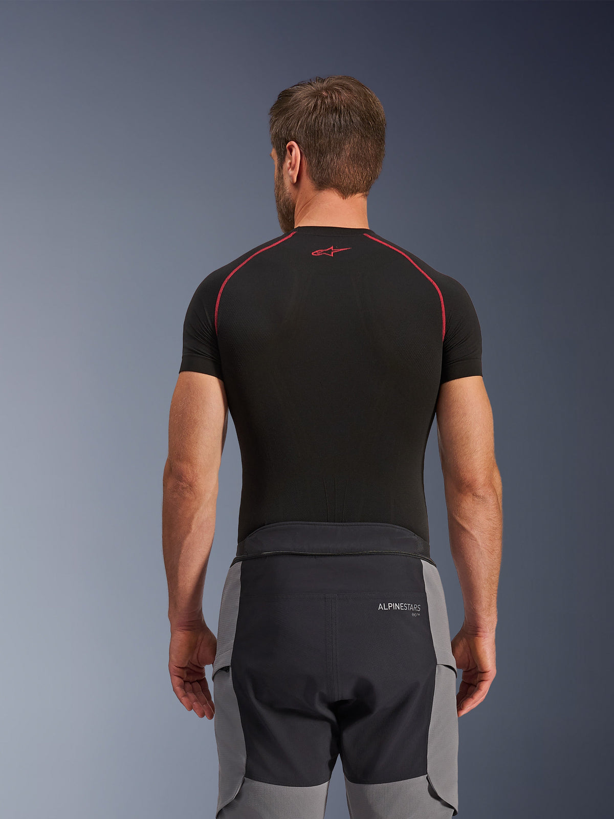 Alpinestars Andes Pro Drystar® XF bukser, adventure motorcykelbukser, mørkegrå og sort, set bagfra med visning af taljekonstruktion og grå sidepaneler, båret med en sort base layer-overdel med røde syninger, teknisk touring-udstyr til al slags vejr