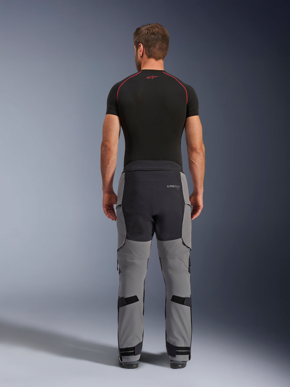 Alpinestars Andes Pro Drystar® XF bukser, adventure motorcykelbukser, mørkegrå og sort, set bagfra, viser grå og sort panelkonstruktion, båret med et sort basislag, med forstærket sæde og justeringsstropper på læggene til touring.