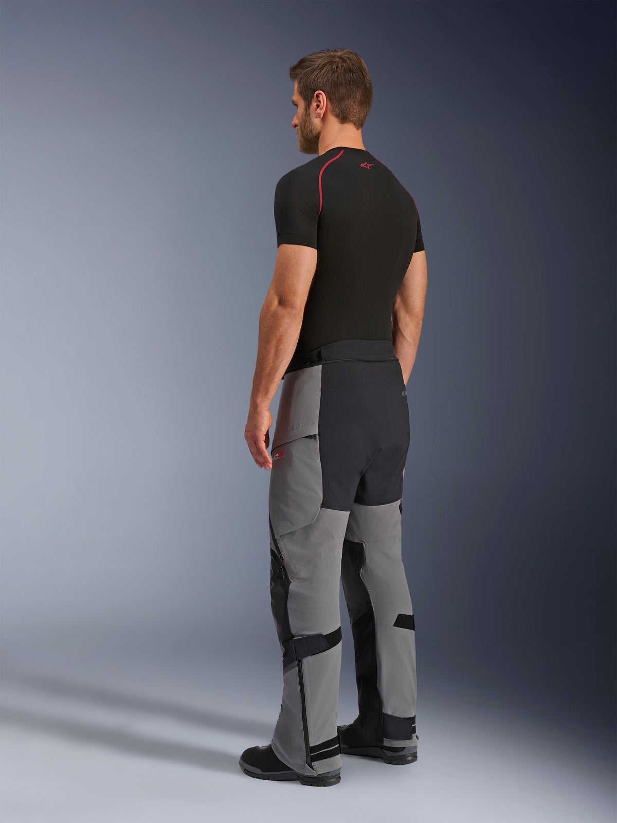 Alpinestars Andes Pro Drystar® XF bukser, adventure-motorcykelbukser, mørkegrå og sort, trefjerdedelsvisning bagfra på model, med teknisk tekstilkonstruktion og sorte forstærkede paneler på sædet og indersiden af benene, vist sammen med en sort base layer t-shirt.