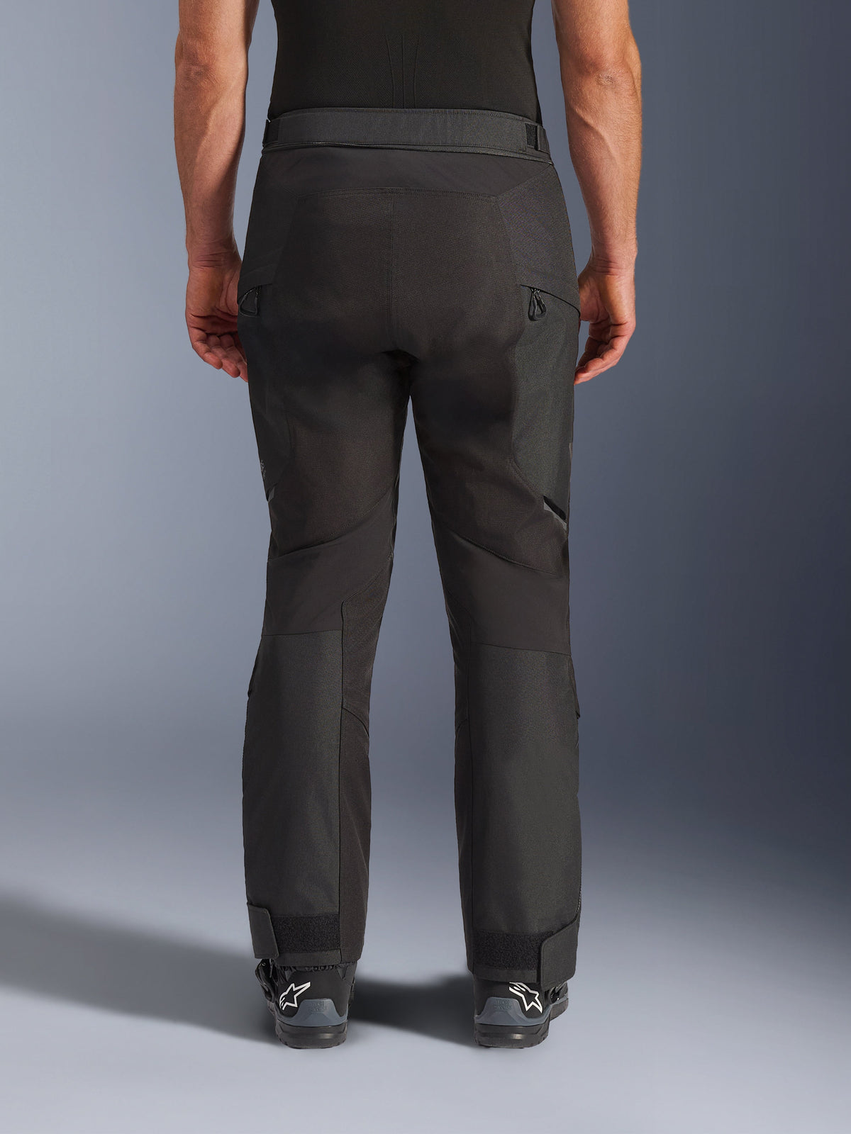 Alpinestars Cusco Drystar® bukser, motorcykelbukser, sort, set bagfra båret af en kører, med teksturerede tekstilpaneler, ventilationsåbninger med lynlås på lårene og justerbare ankellukninger, kombineret med sorte Alpinestars-støvler.