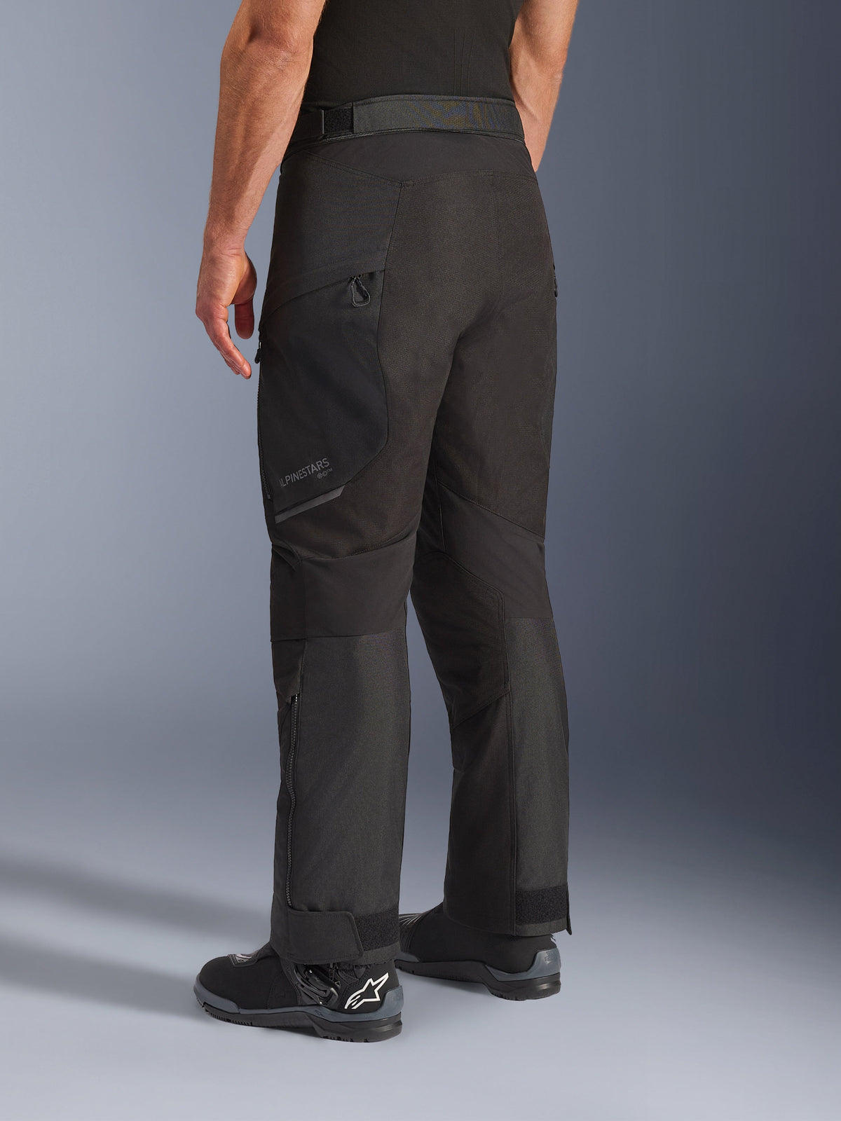 Alpinestars Cusco Drystar® bukser, motorcykelbukser, sort, trekvart visning bagfra med lårlomme med lynlås og formsyede paneler, båret med sorte motorcykelstøvler, slidstærkt adventure touring-design med diskret branding