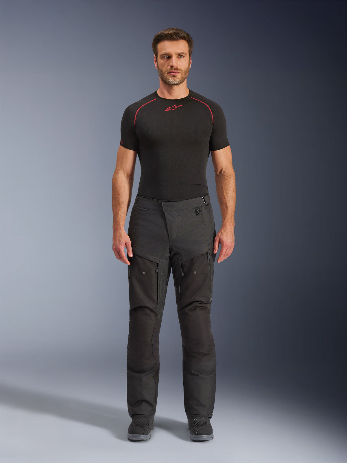 Alpinestars Cusco Drystar® bukser, tekstil motorcykelbukser, sorte, båret af en model med et sort basislag og støvler, adventure touring-design med lårventilationspaneler med lynlås og en holdbar konstruktion med flere paneler