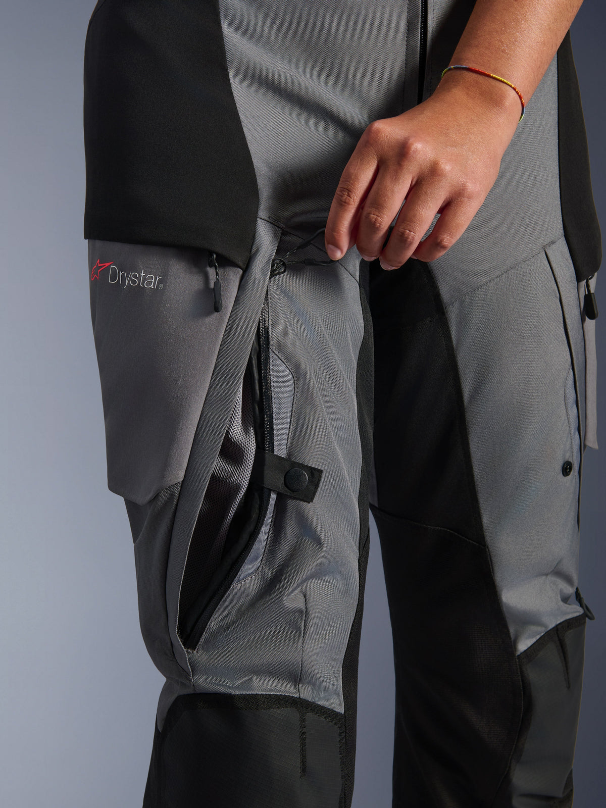 Alpinestars Stella Andes V4 Drystar bukser, sort og mørkegråt tekstil, nærbillede af ventilationslynlås på låret der åbnes med hånden, synligt mesh-for, Drystar-logo, adventure motorcykeludstyr
