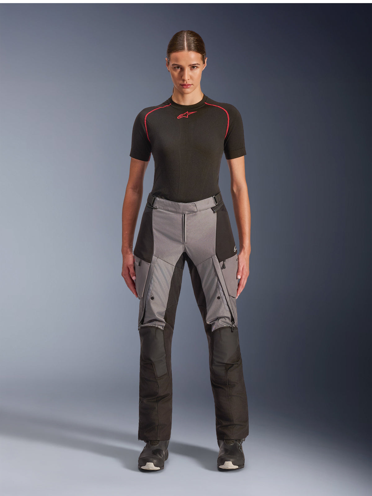 Alpinestars Stella Andes V4 Drystar bukser, eventyr-touring motorcykelbukser til kvinder, sort og mørkegrå, båret af en kvindelig model med et sort basislag og motorcykelstøvler, med forstærkede tekstilpaneler og cargolommer til eventyrkørsel
