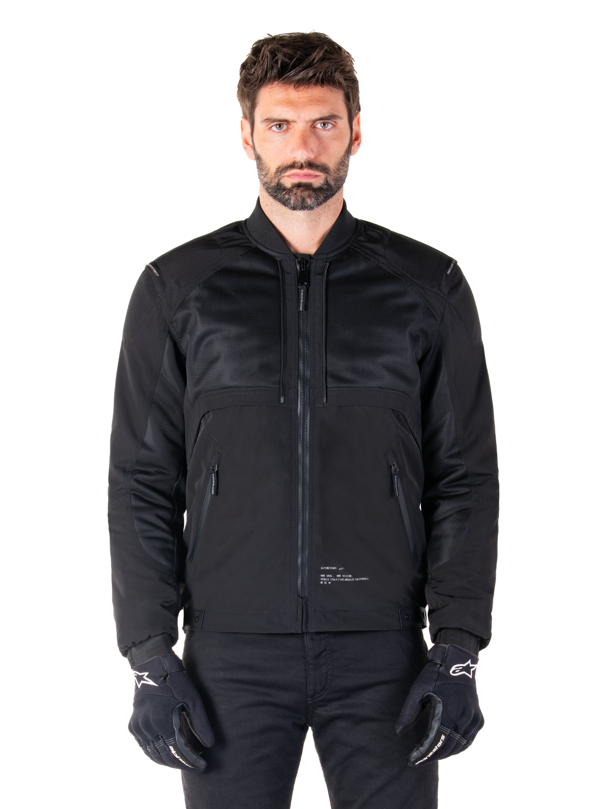 Alpinestars Mootant Vandtæt Parka, sort motorcykeljakke, set forfra på mandlig model, med modulær tekstilkonstruktion med mesh-paneler til ventilation, ribbet krave og lynlåslommer, båret med sorte handsker med hvid Alpinestars-branding