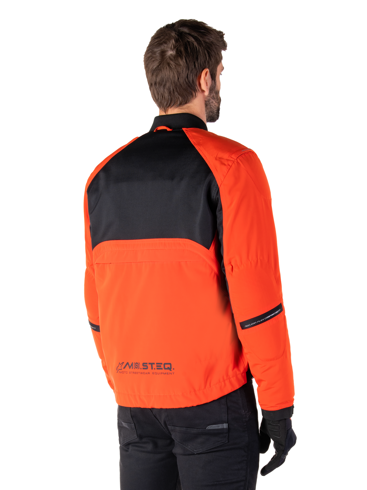 Rear view of a rider wearing the Alpinestars Mootant Waterproof Parka in Spicy Orange and Black, featuring a black mesh upper back panel and reflective MO.ST.EQ. branding, modern utilitarian motorcycle jacket.