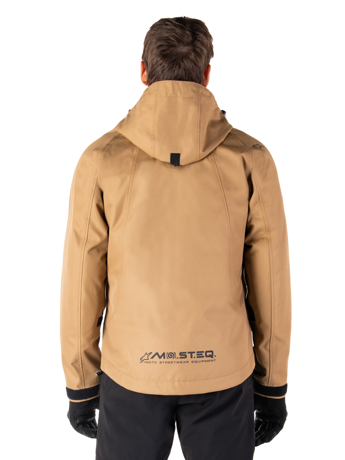 Alpinestars Morush Waterproof Parka, Utility Brown, rear view, featuring a hood and MO.ST.EQ. branding on the lower back, paired with black pants and gloves, modern streetwear-inspired motorcycle gear
