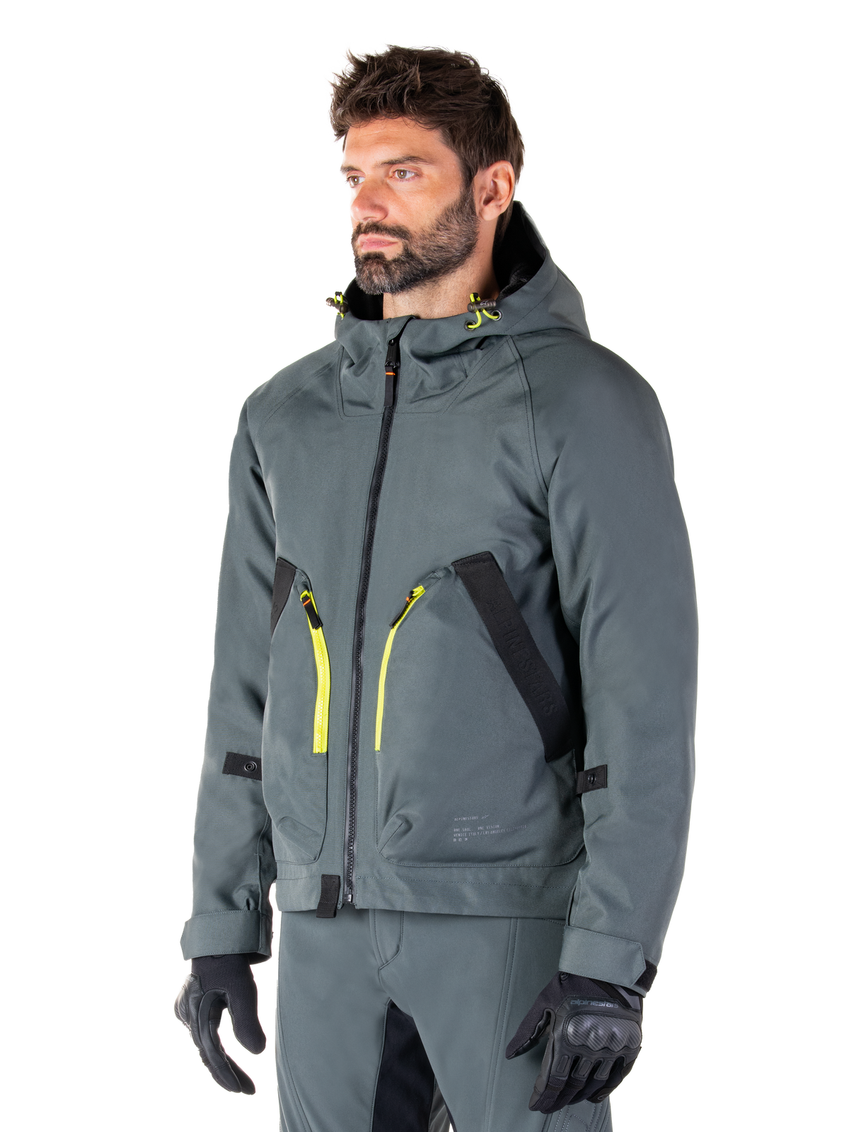 Alpinestars Morush Waterproof Parka, Urban Gray motorcykeljakke, design med hætte og klare gule lynlåsdetaljer, sorte lommedetaljer, båret med matchende grå kørebukser og sorte handsker, moderne streetwear-inspireret motorcykelbeklædning.