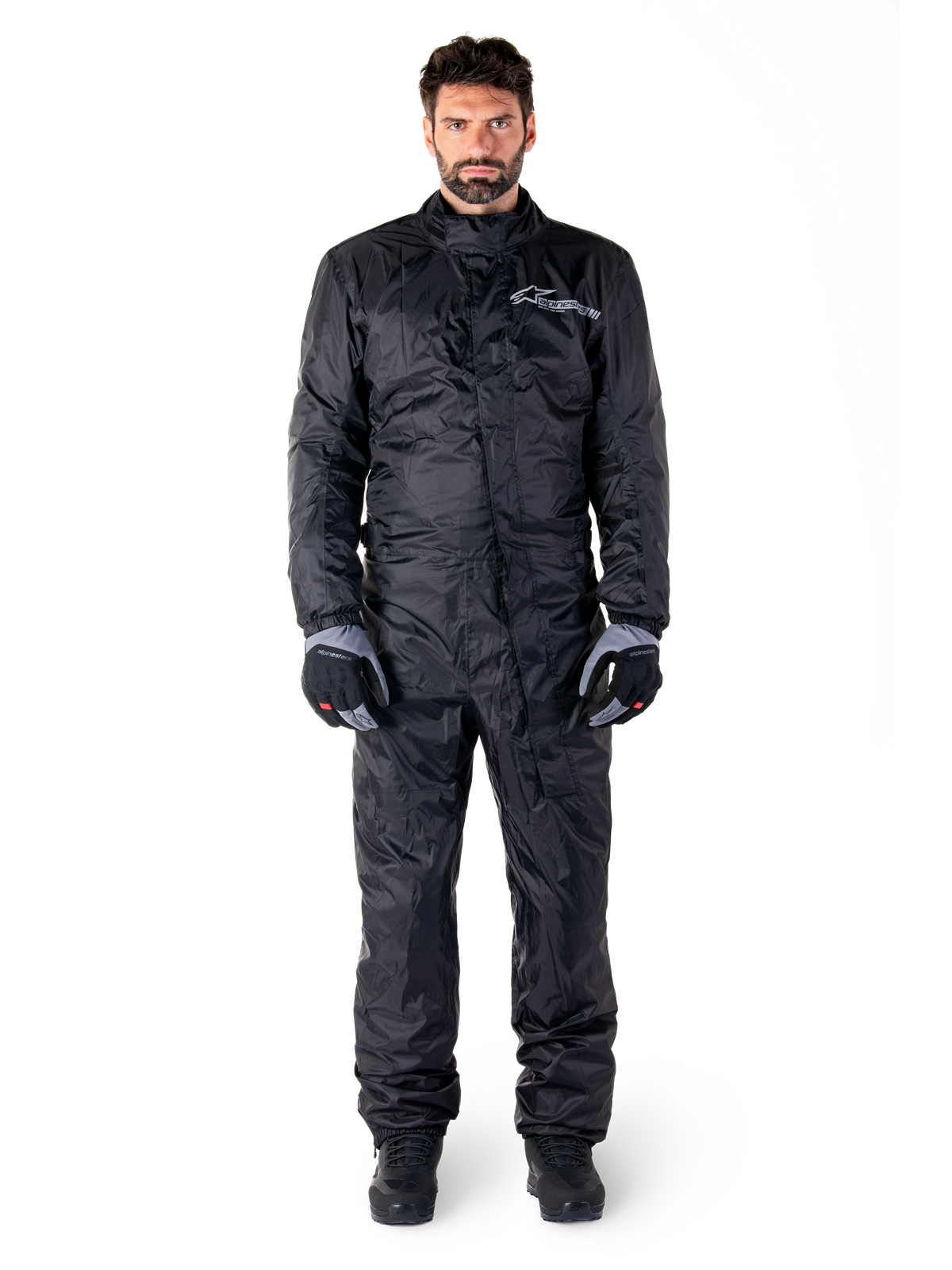 Alpinestars Hurricane Rain V2 Suit, sort helkrops-regndragt til motorcykel, vandtæt beskyttelsesudstyr med høj krave og stormlukning foran, hvidt logo på brystet, båret med sorte og grå handsker og støvler