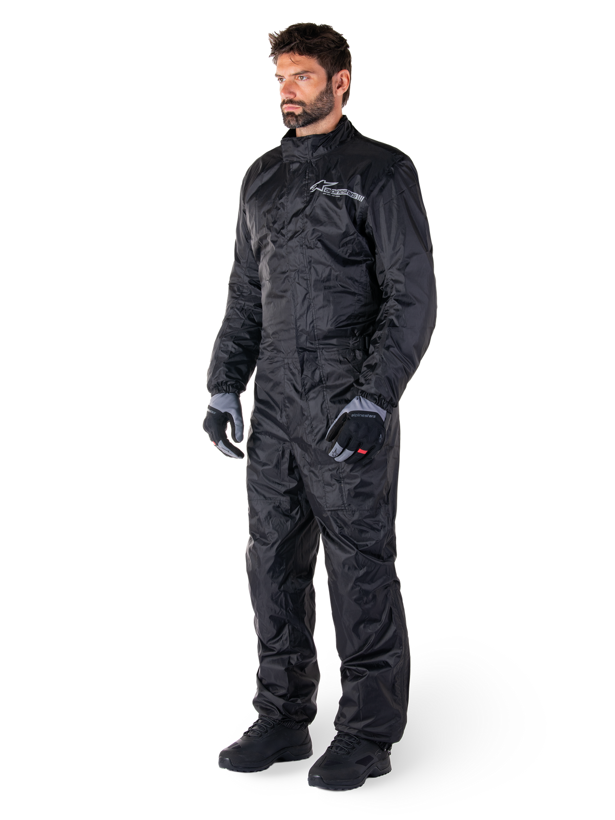 Alpinestars Hurricane Rain V2-dragt, sort, vandtæt motorcykel-regndragt i ét stykke, båret med handsker og støvler, med reflekterende Alpinestars-branding på brystet, letvægtsdesign til beskyttelse i vådt vejr