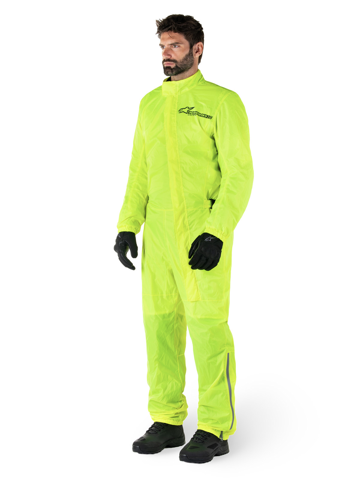 Alpinestars Hurricane Rain V2-dragt, vandtæt motorcykelregndragt i ét stykke, gul fluo, båret med sorte handsker og støvler, med et sort Alpinestars-logo på brystet og reflekterende detaljer på benene