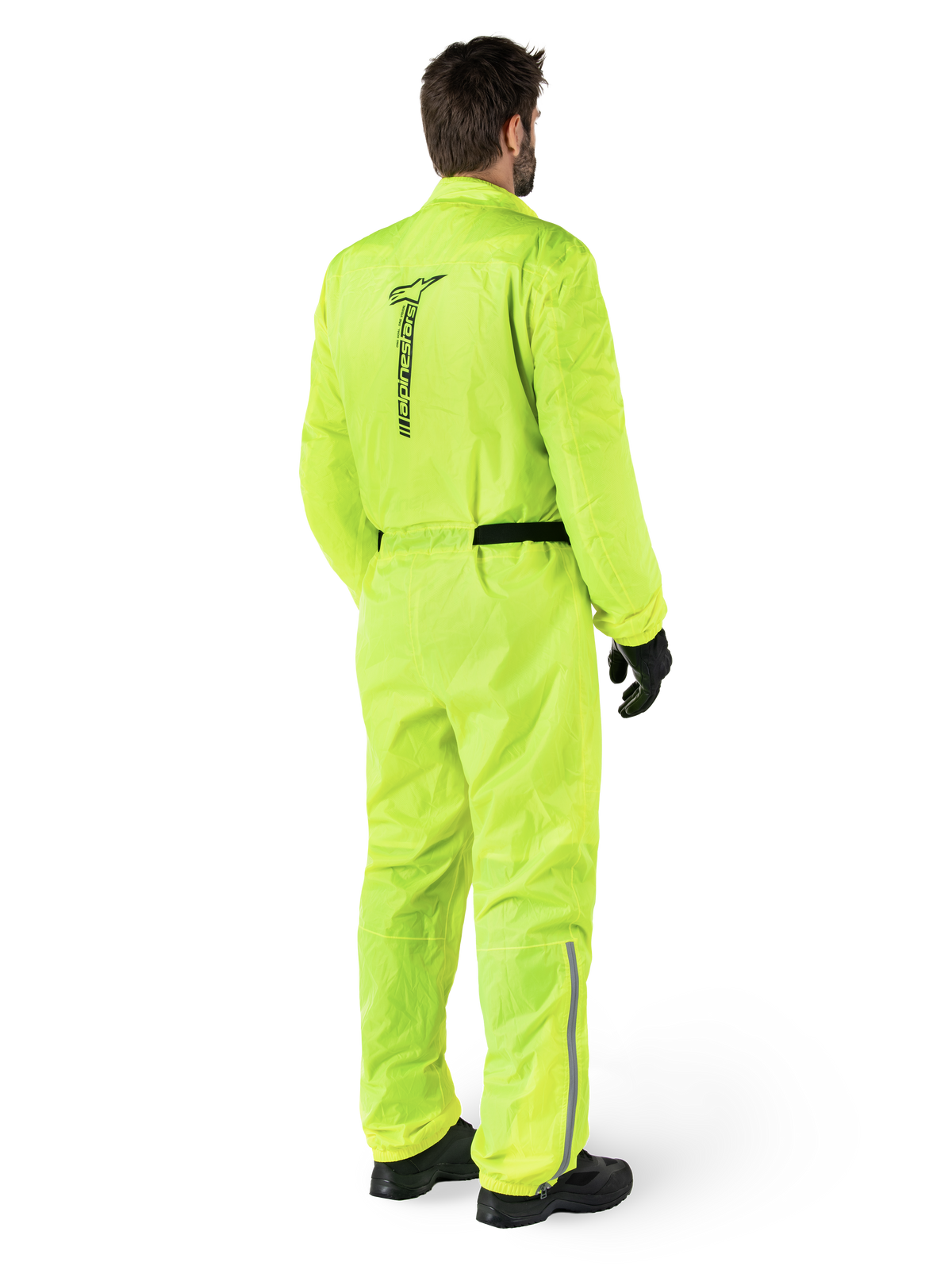 Alpinestars Hurricane Rain V2-dragt, Yellow Fluo, set bagfra af en kører iført en motorcykel-regndragt i ét stykke, med et sort Alpinestars-logo på ryggen, sort taljebælte og refleksstriber på underbenene, båret med sorte handsker og støvler
