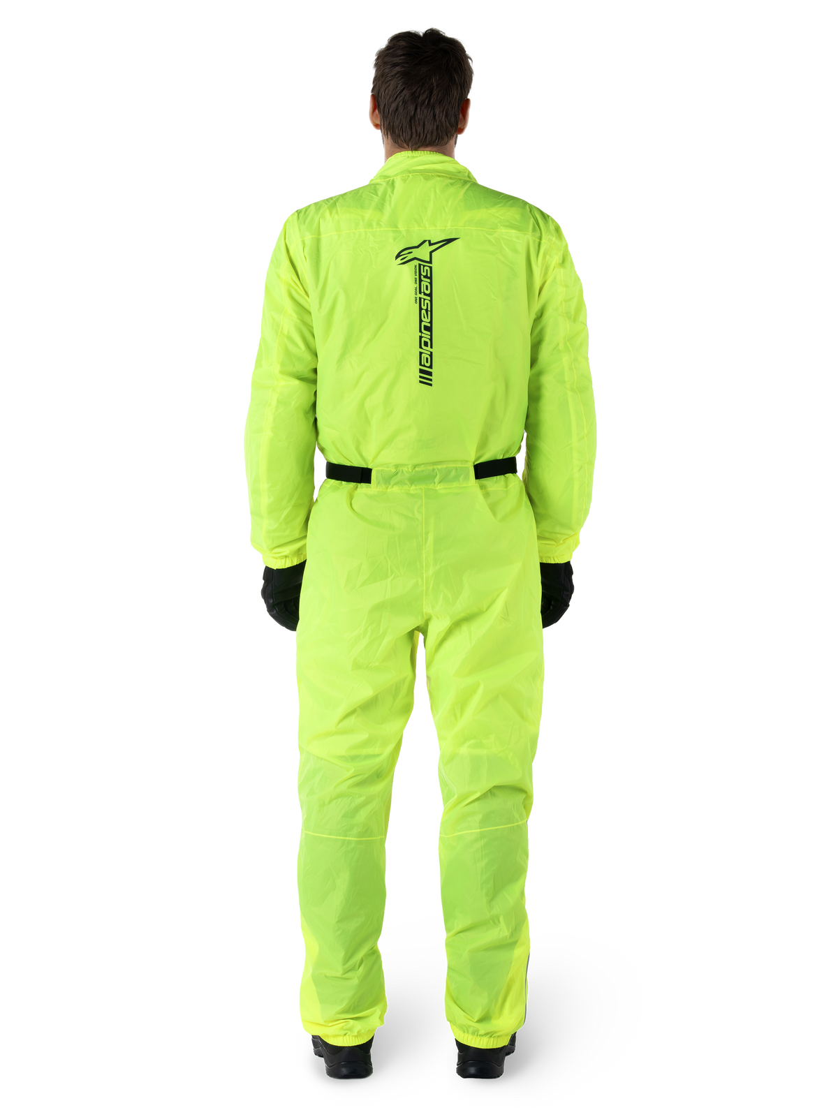 Alpinestars Hurricane Rain V2-dragt, motorcykelregndragt i ét stykke, gul fluo, set bagfra med lodret sort Alpinestars-branding, elastik i taljen og ved manchetterne, båret med sorte handsker og støvler, vandtæt og vindafvisende køreudstyr