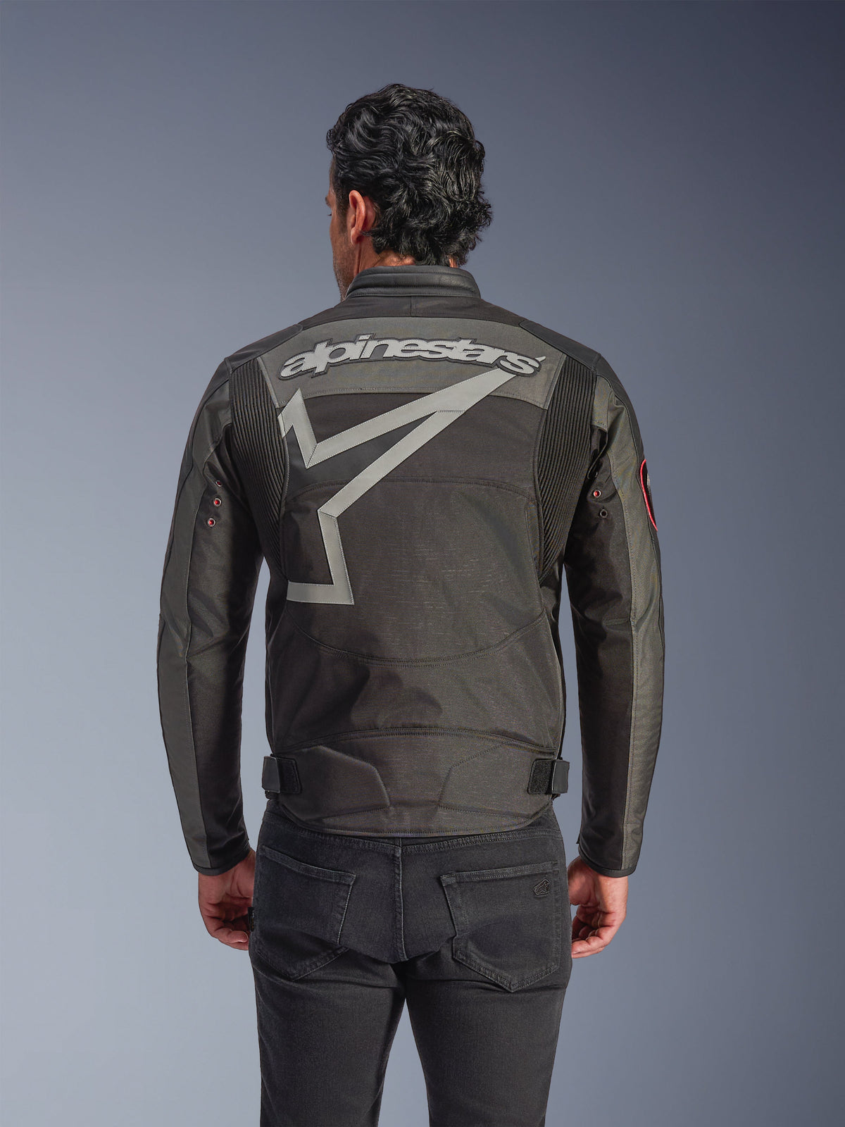 Alpinestars Axton Jacket, Men's Motorcycle Jacket, Black Anthracite Red Tangerine, back view featuring a large grey Alpinestars wordmark and stylized star graphic, accordion shoulder panels, and vintage-inspired metal eyelets on the sleeves.