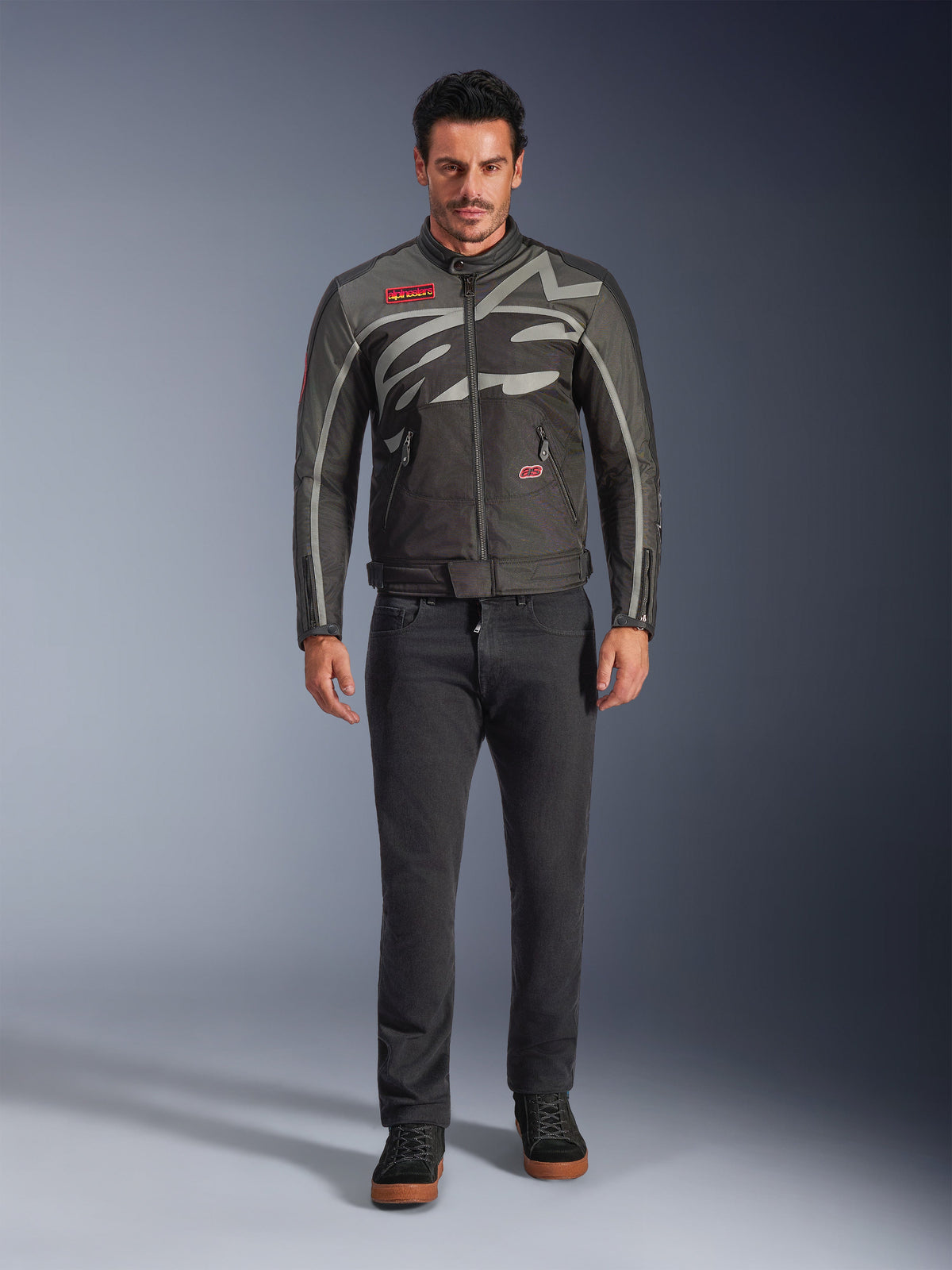 Alpinestars Axton Jacket, Motorcycle Jacket, Black Anthracite Red Tangerine, worn by a model with dark pants, featuring a wrap-around gray Alpinestars logo, red brand patches, and a water-resistant textile shell for urban road riding