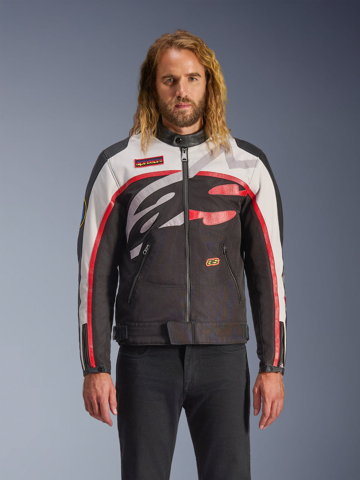 Alpinestars Axton Jacket, Motorcycle Jacket, Black Off White and Bright Red, featuring bold abstract chest patterns and wrap-around logo, red striped sleeves, vintage-inspired design with a minimalist collar, worn by model with black jeans.