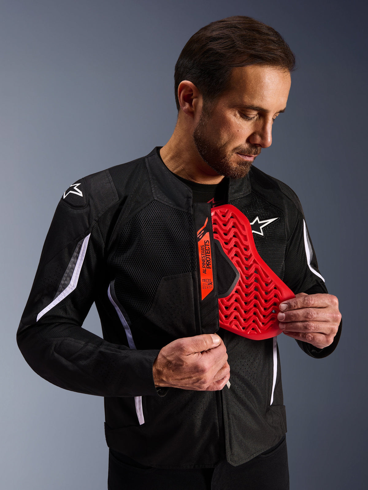 Alpinestars AST V3 Air-jakke i sort, mand der viser et klart rødt brystbeskytter-indlæg med bikagemønster, fremhæver Tech-Air Ready-kompatibilitet og integreret indvendig beskyttelse til motorcykelsikkerhed.