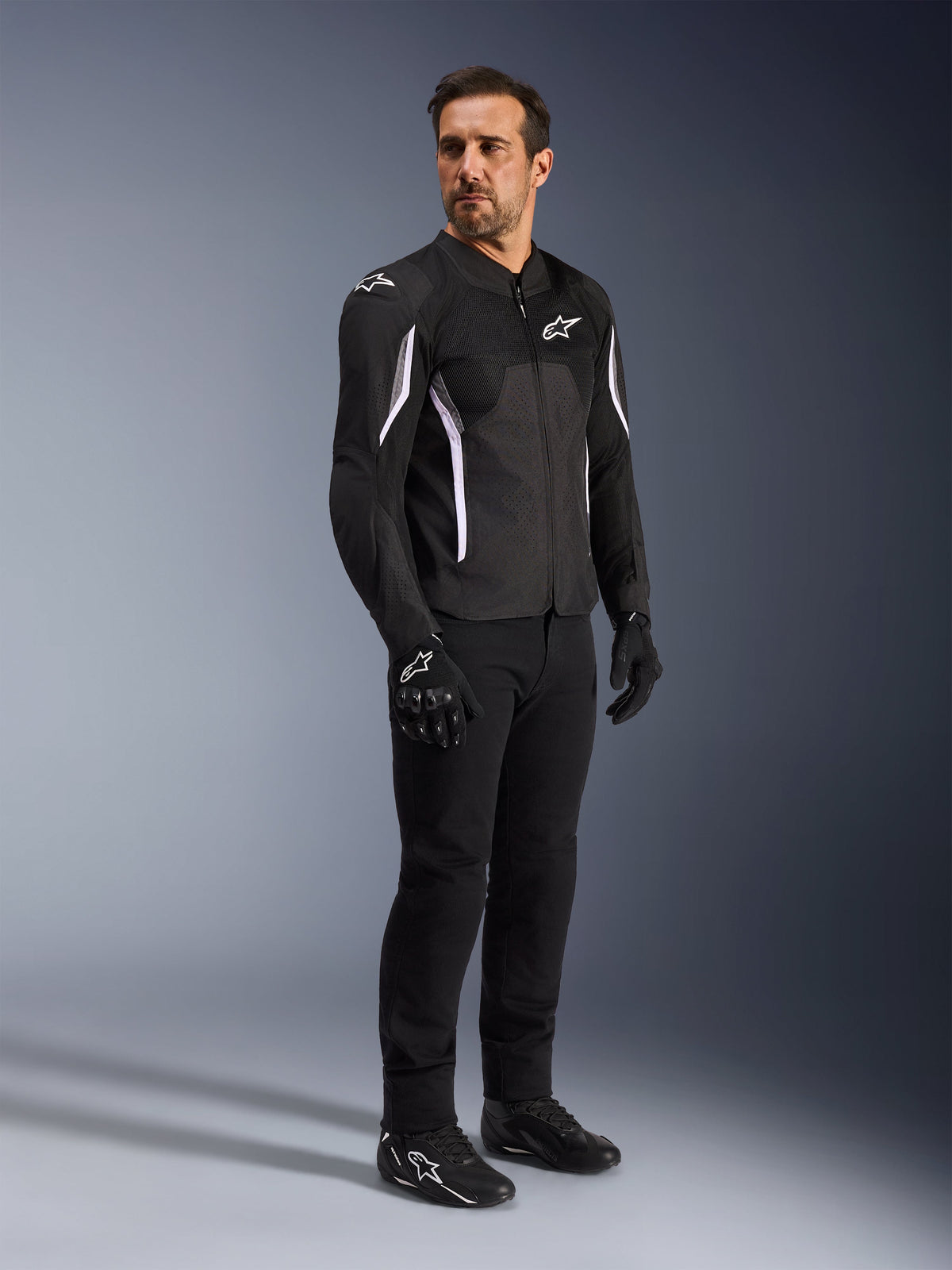 Alpinestars AST V3 Air-jakke, sort med hvide detaljer og logoer, letvægts motorcykeljakke med mesh-ventilation, båret af en mand med sorte kørebukser, handsker og sko, teknisk sommerudstyr til sport og street