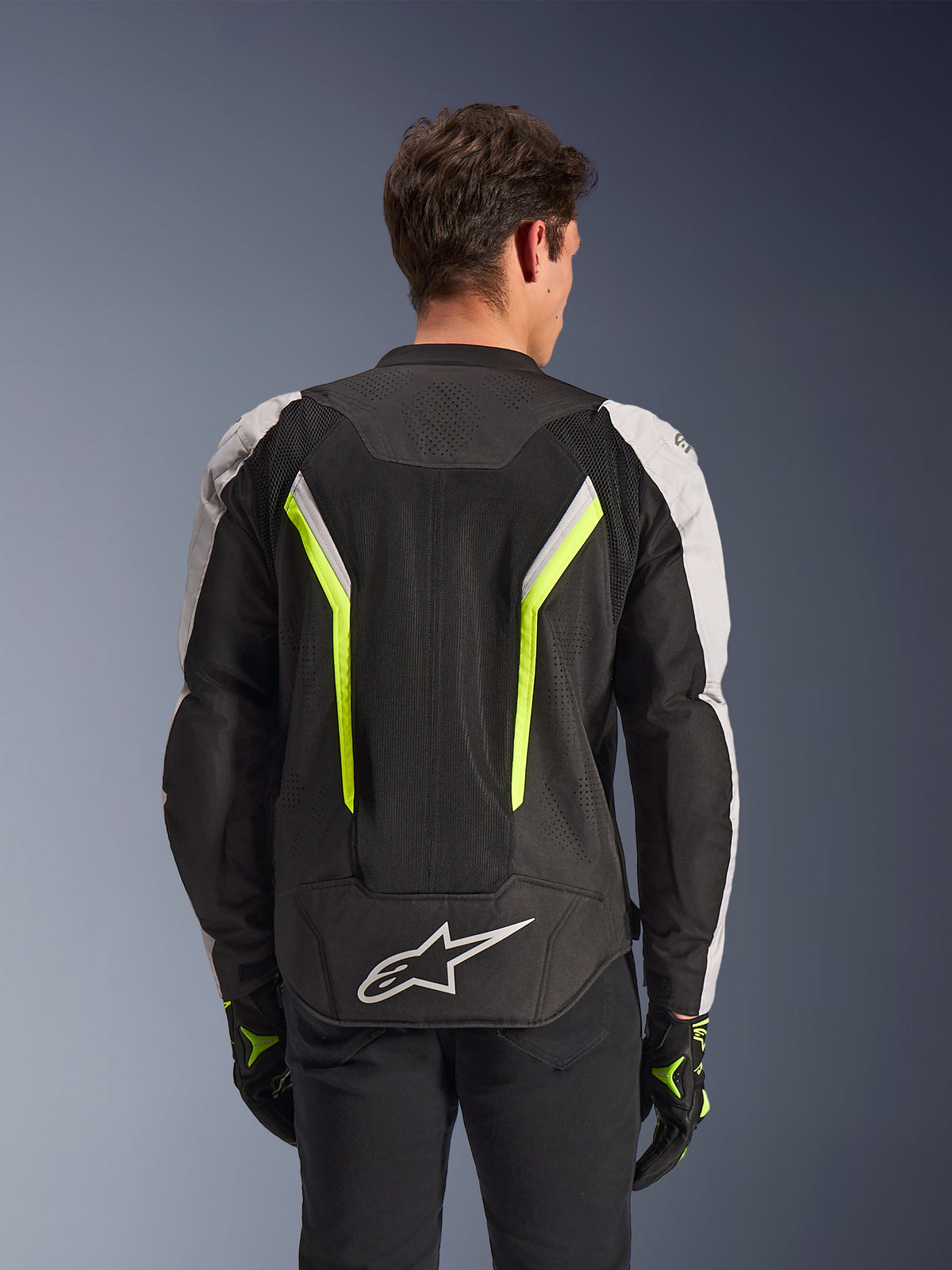 Alpinestars AST V3 Air Jacket, tekstil motorcykeljakke, Black Silver Yellow Fluo, set bagfra på model, dobbelte tech mesh-ventilationspaneler, lodrette neongule striber, sølvfarvede ærmer og hvidt Alpinestars-logo på lænden.