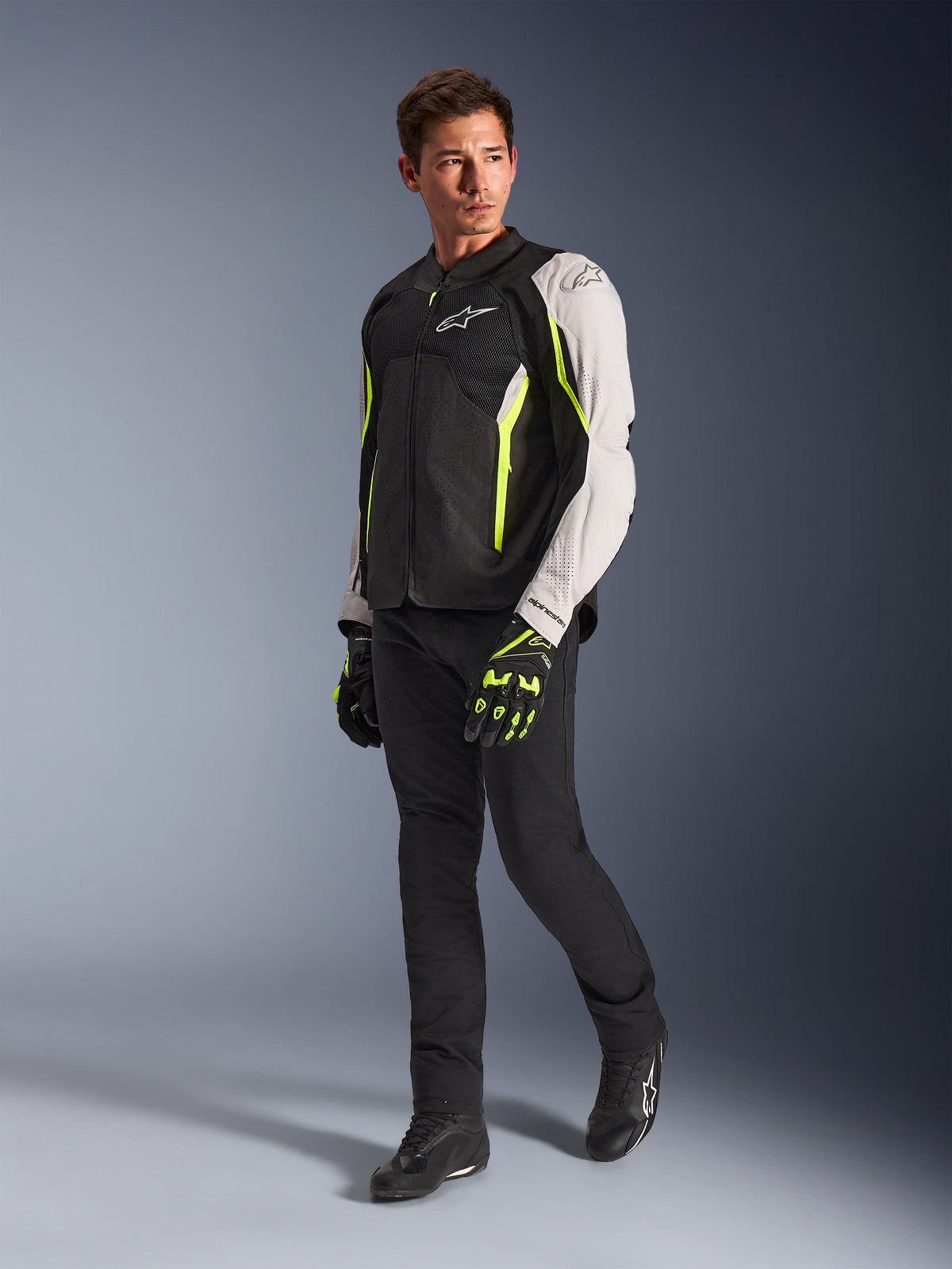 Alpinestars AST V3 Air Jakke, let tekstil motorcykeljakke i sort, sølv og gul fluo, båret af en model med sorte bukser og matchende handsker, med mesh-paneler og laserperforeringer til sportskørsel i varmt vejr.