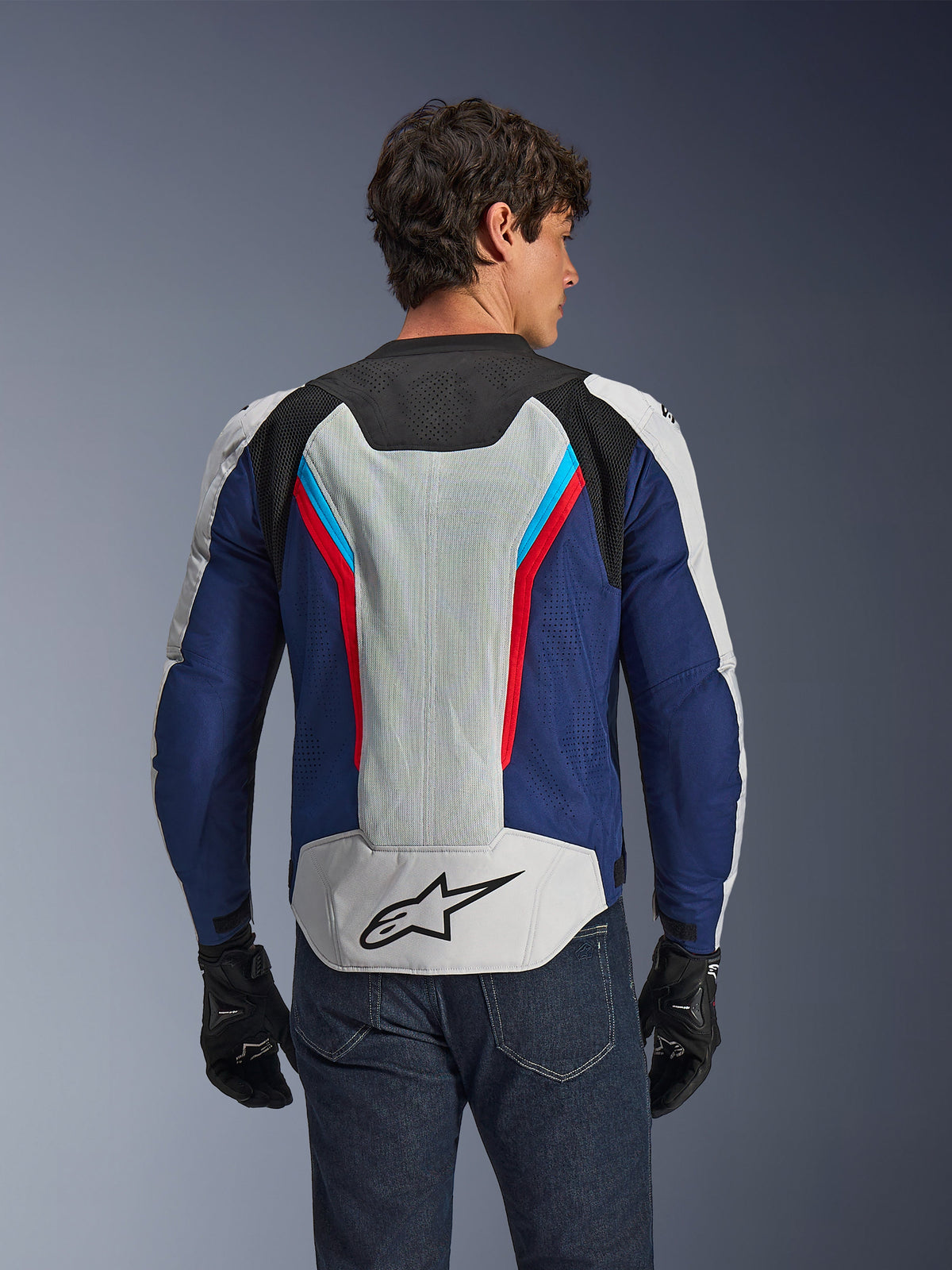 Alpinestars AST V3 Air jakke, motorcykeljakke, Silver Deep Blue Bright Red, set bagfra på en kører, med tech mesh-paneler og laserperforeringer for ventilation, sort stjernelogo på den nedre del af ryggen, sportsoptimeret design til varmt vejr