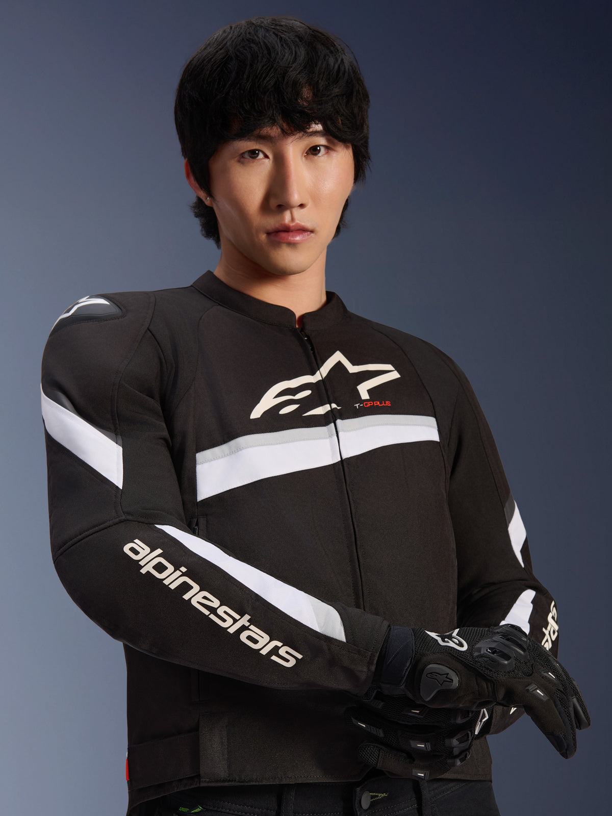 Alpinestars T-GP Plus R V4 Jacket, Black and White, worn by a male model, textile motorcycle jacket with white stripes across the chest and sleeves, Alpinestars logo on the chest, paired with black riding gloves