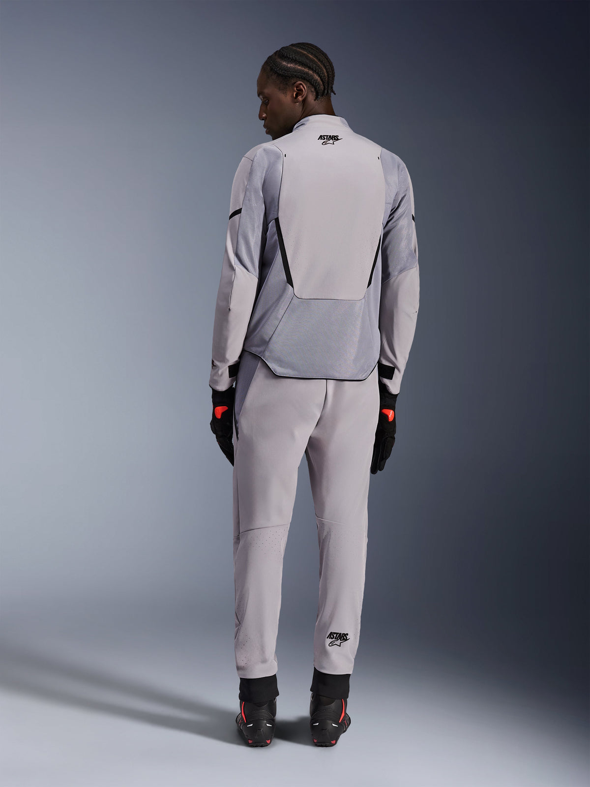 Alpinestars Aeroshell Airflow Jakke, Mid Gray Anthracite, set bagfra på en model, med tekniske mesh-paneler og laserperforerede ventilationszoner, båret med matchende grå bukser og sort motorcykeludstyr, sport-cut design til høj ydeevne.