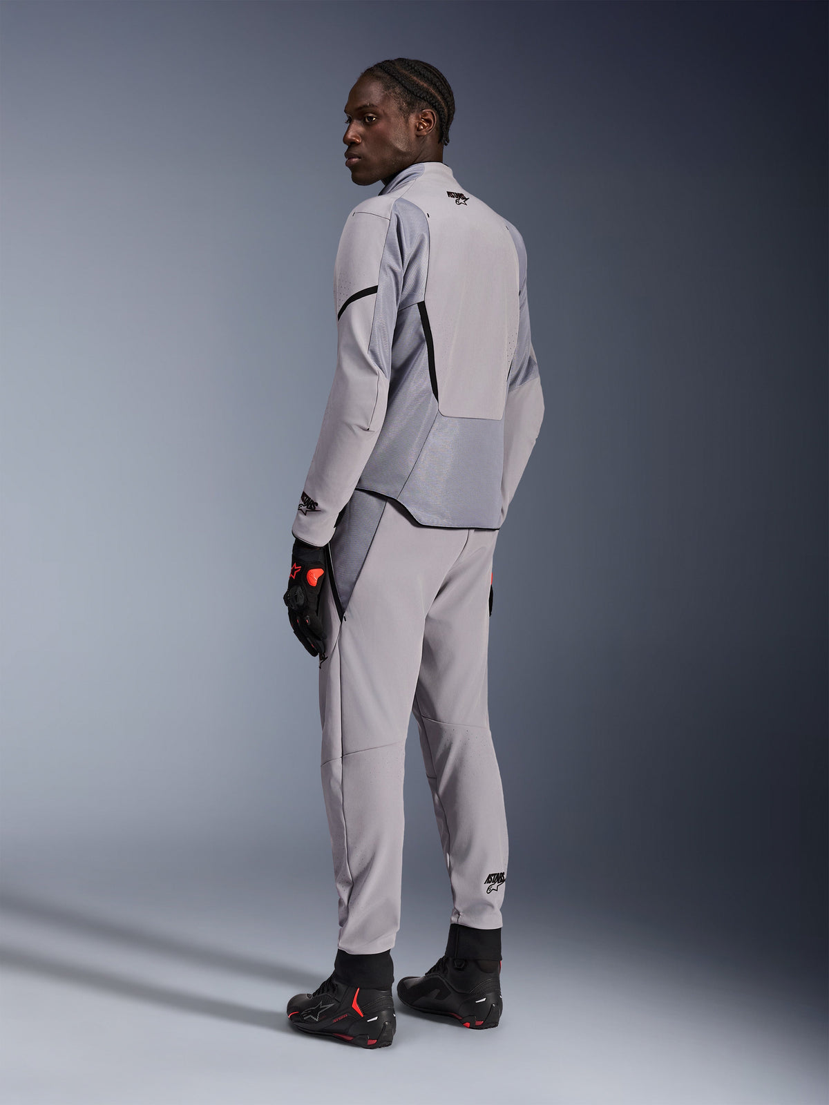 Alpinestars Aeroshell Airflow-jakke i Mid Gray Anthracite, båret med matchende bukser og sorte racinghandsker, set bagfra med laserperforerede paneler og atletisk sportspasform, professionel motorcykelbeklædning