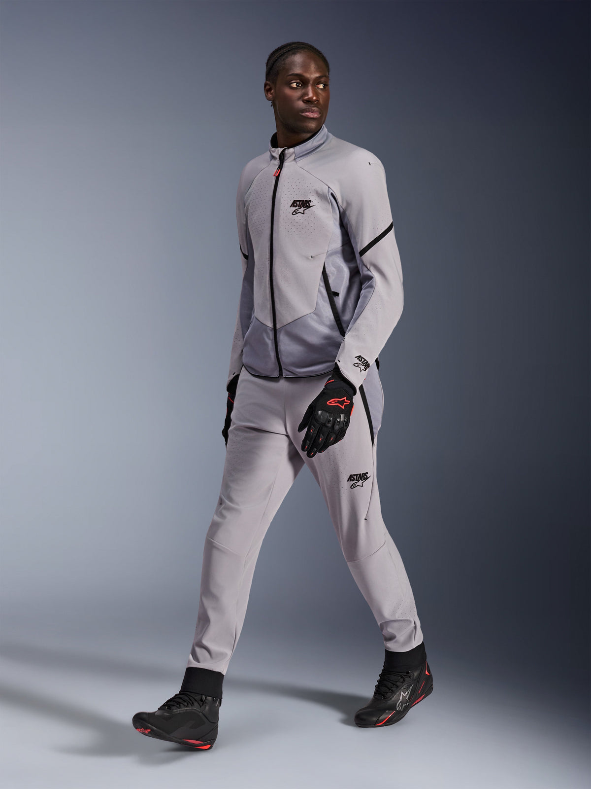 Alpinestars Aeroshell Airflow-jakke i Mid Gray Anthracite, båret af en mandlig model med matchende grå kørebukser og sorte handsker, med laserperforeret brystventilation og et strømlinet sport-cut design.
