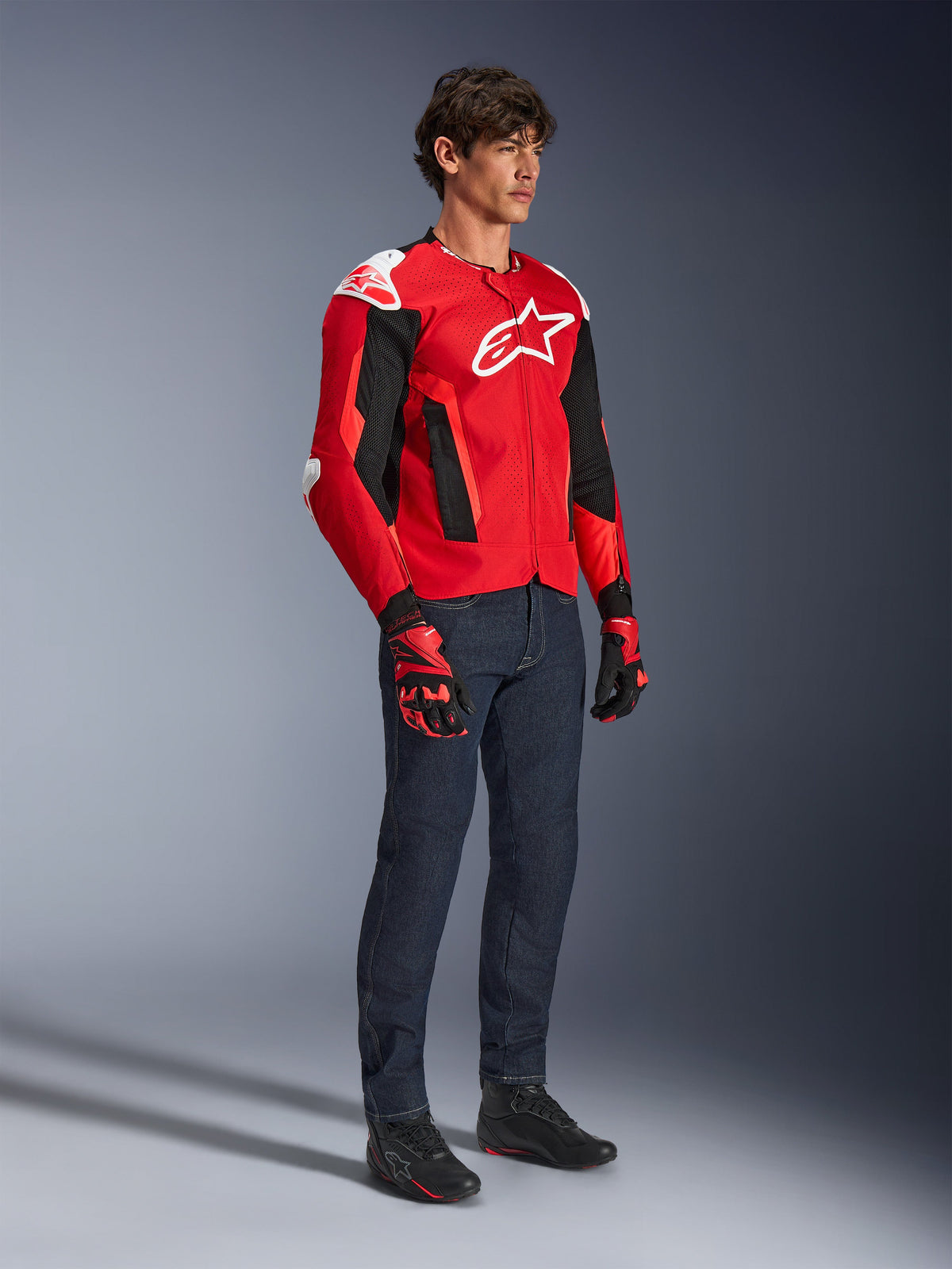 Alpinestars T-GP Air-jakke, sportsmotorcykeljakke, stærk rød og sort med hvide detaljer, båret af en model med mørkeblå jeans og røde racerhandsker, med high-flow mesh-paneler og hvide skulder-sliders, aerodynamisk sportspasform til kørsel i varmt vejr.